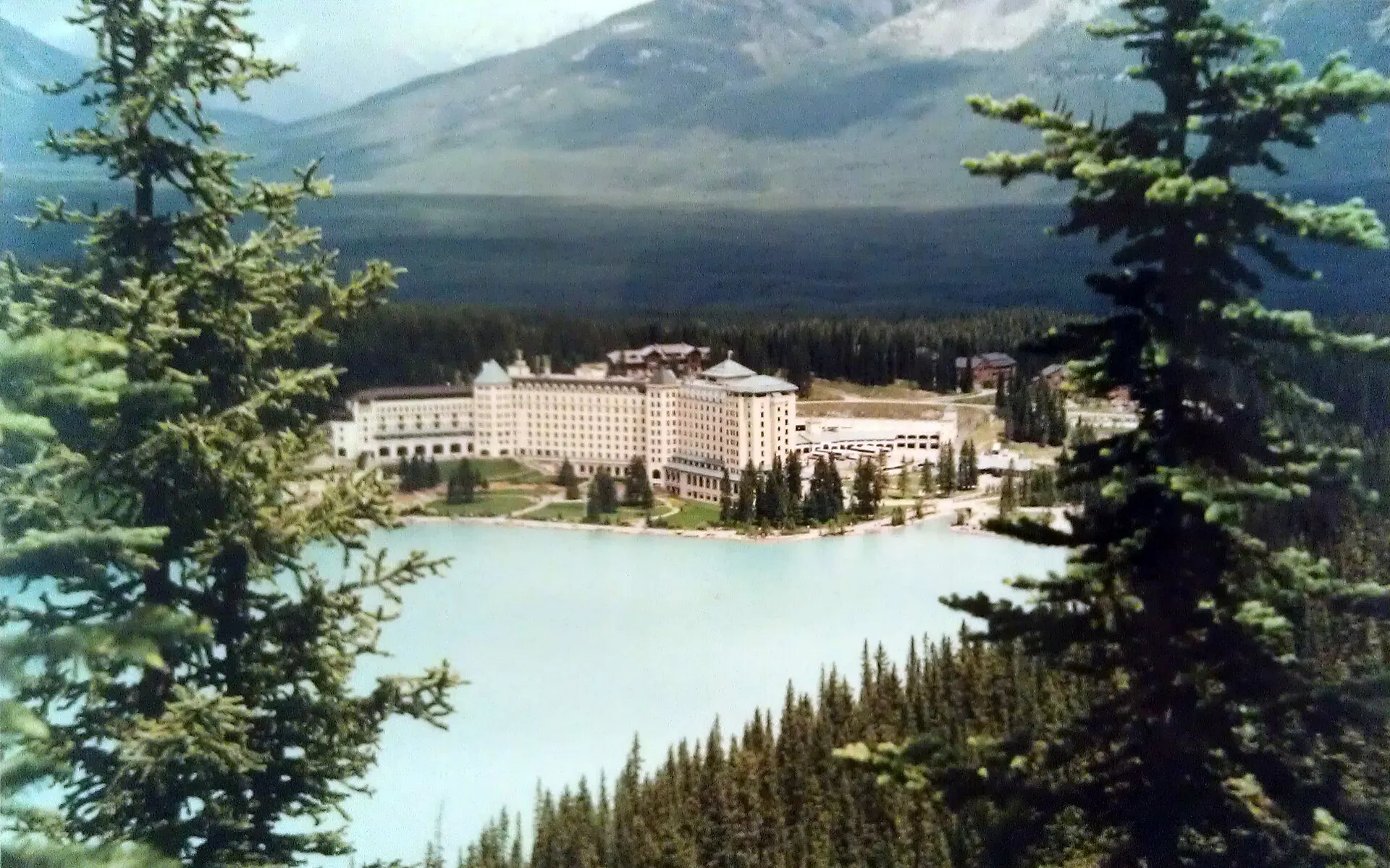 Large hotel on the shore of a turquoise mountain lake framed by evergreen trees