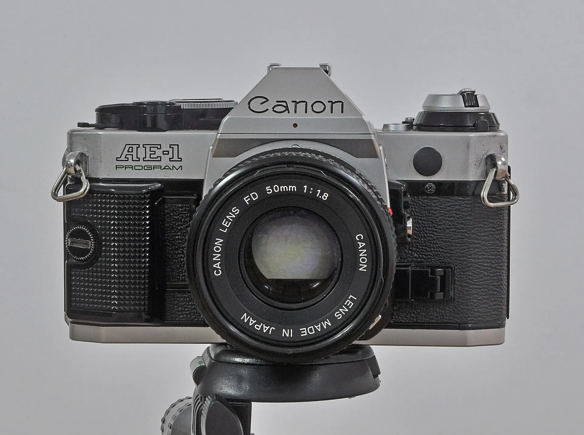 Chrome Canon AE-1 Program seen from the front with a Canon FD 50mm f/1.8 lens, on a plain gray background