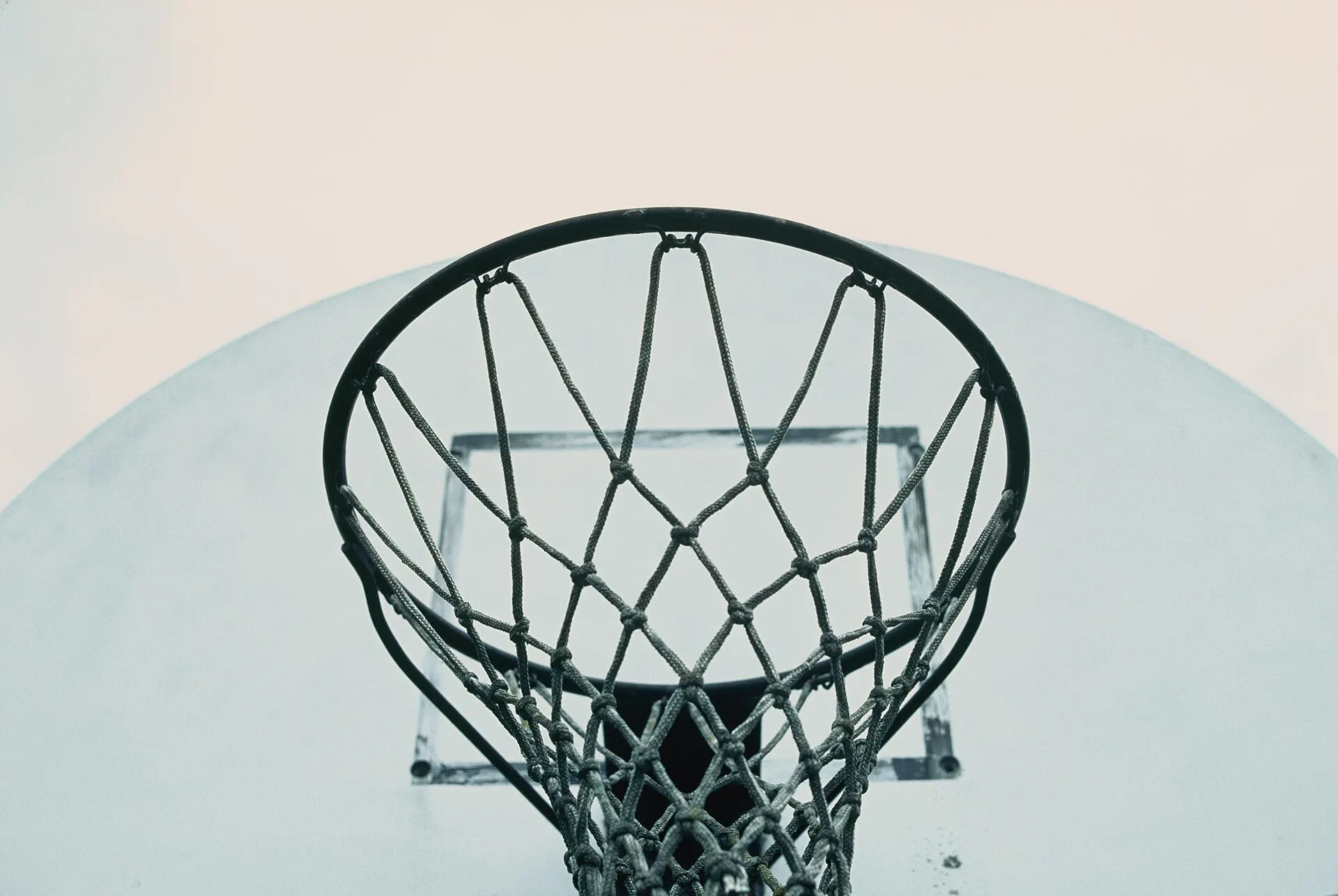 Basketball hoop and net seen from below against a pale sky