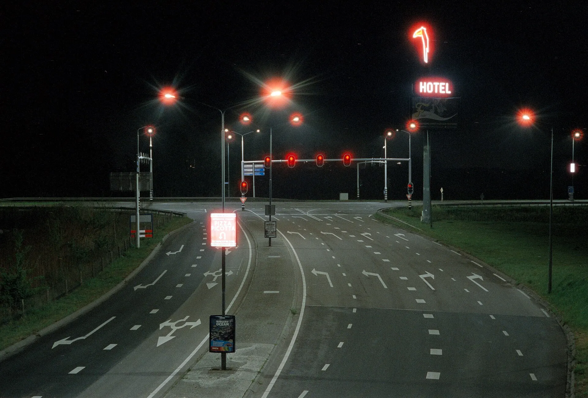 Long exposure of an empty road at night, streetlights and a red hotel sign glowing in the dark