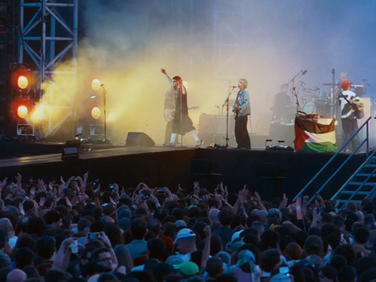 A band on stage under orange and yellow stage lights and haze, with the festival crowd in the foreground