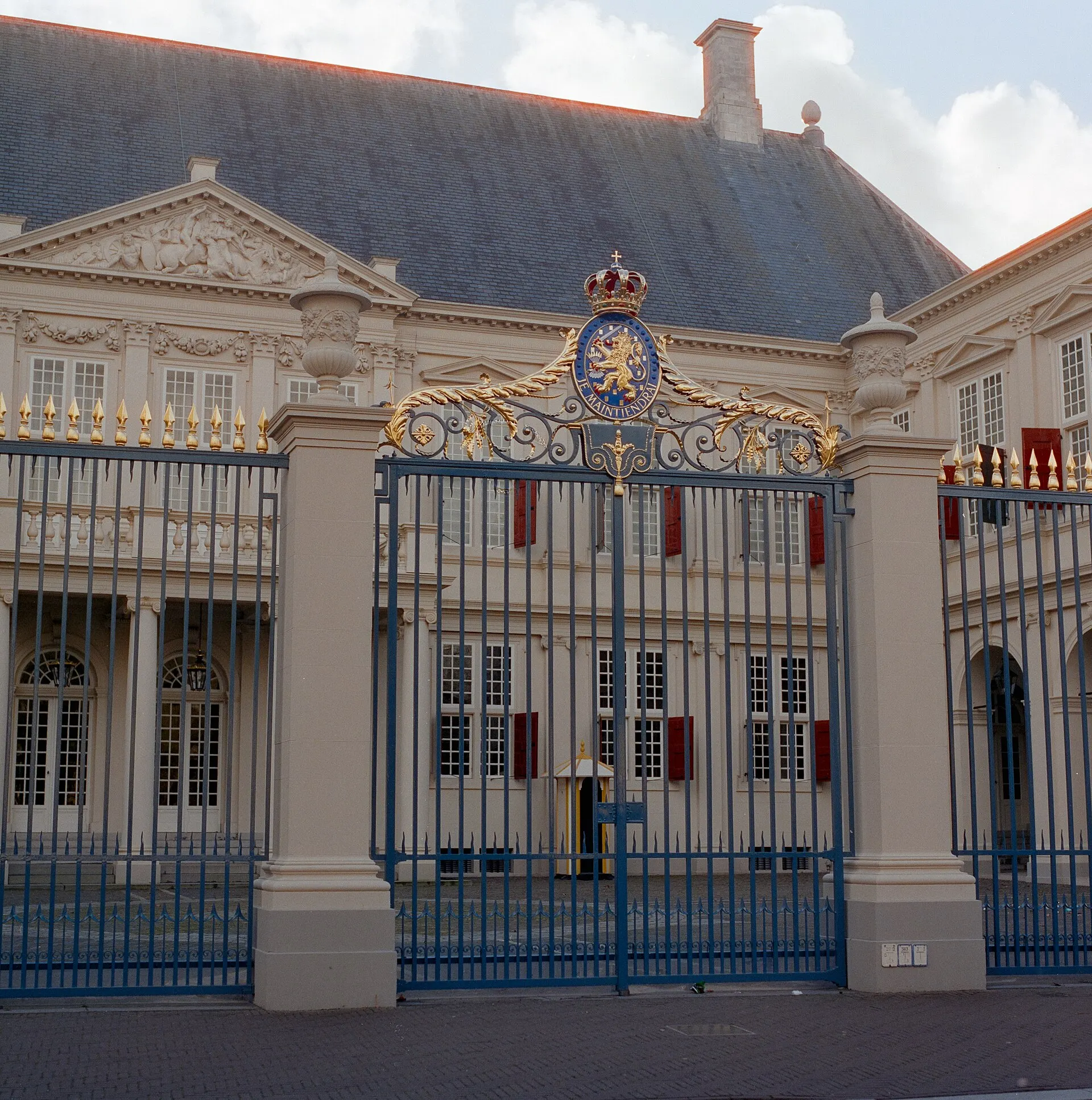The ornate gate of Paleis Noordeinde with a gold crest above dark iron railings, shot in daylight
