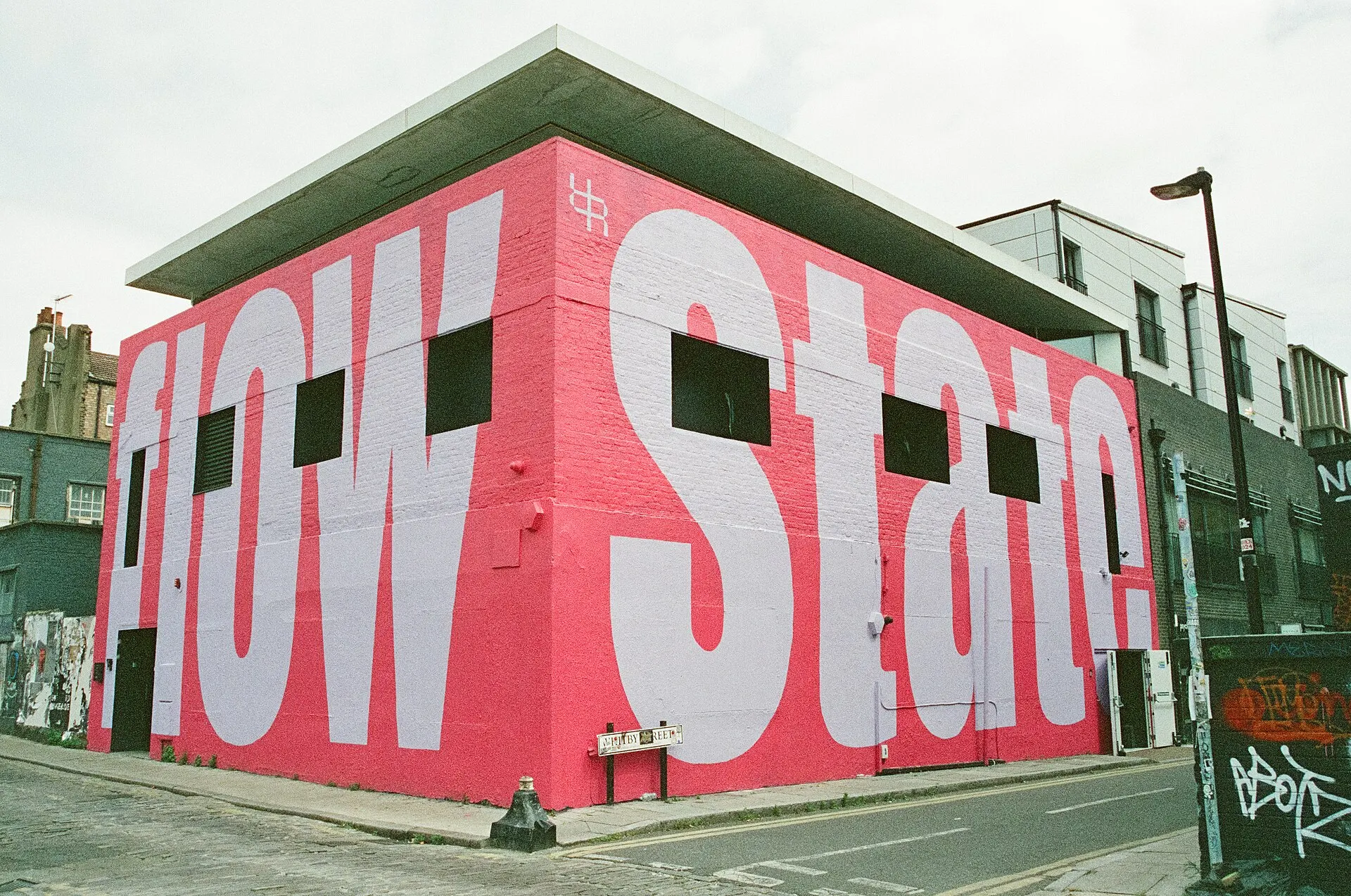 A pink building painted with giant white letters on a London street corner, shot in daylight