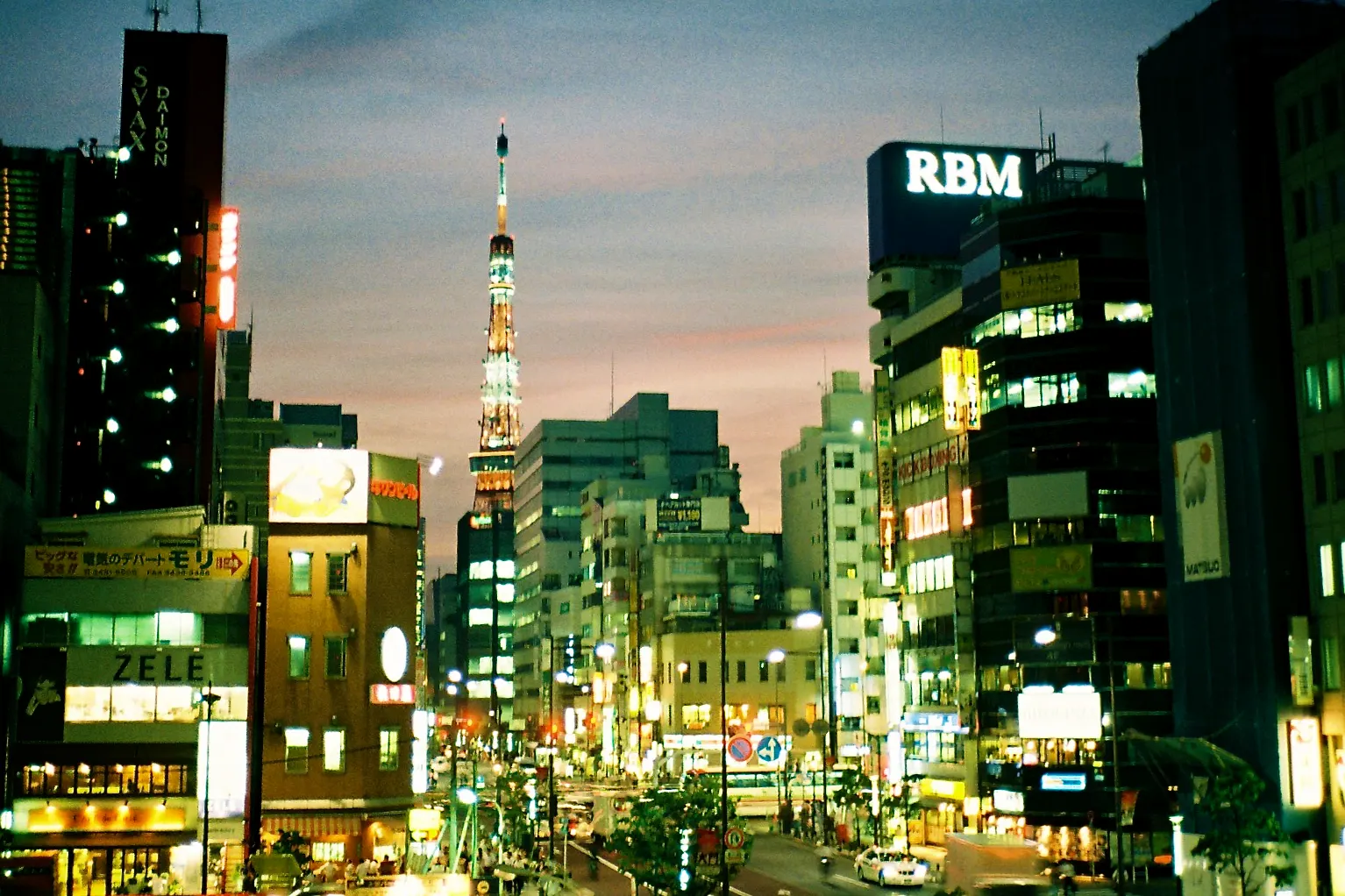 Tokyo Tower lit at dusk above a street of shops and office buildings
