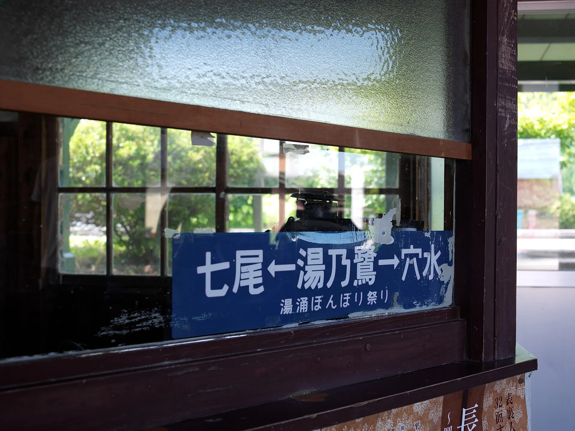 Station waiting room window with a blue Japanese station name sign