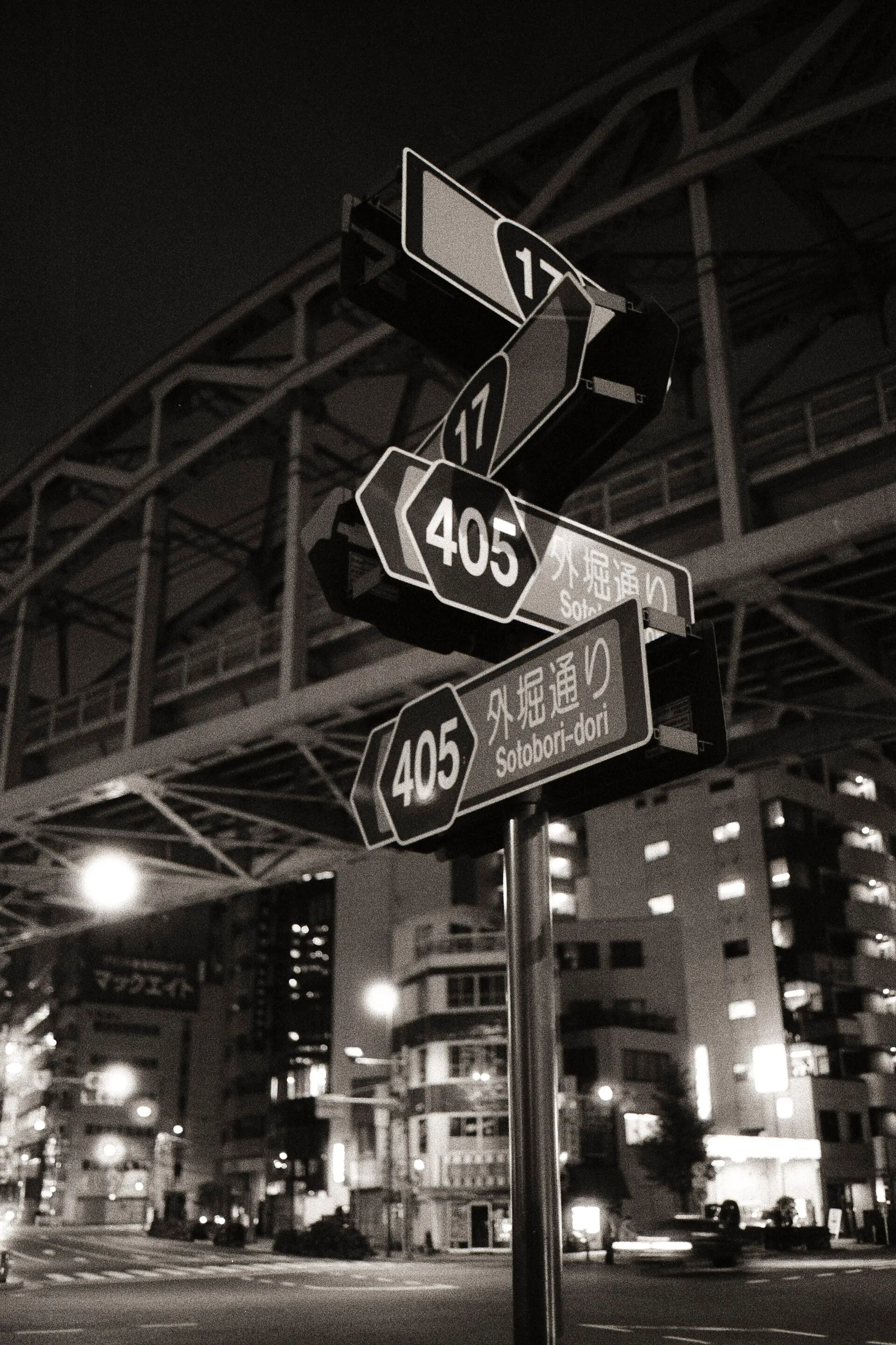 Night crossroads under an elevated railway in Akihabara, with route signs 17 and 405 lit by street lamps
