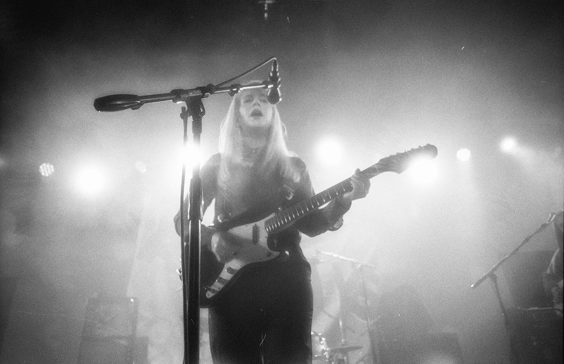 A singer with a guitar on a dark stage, backlit by bright stage lights and haze