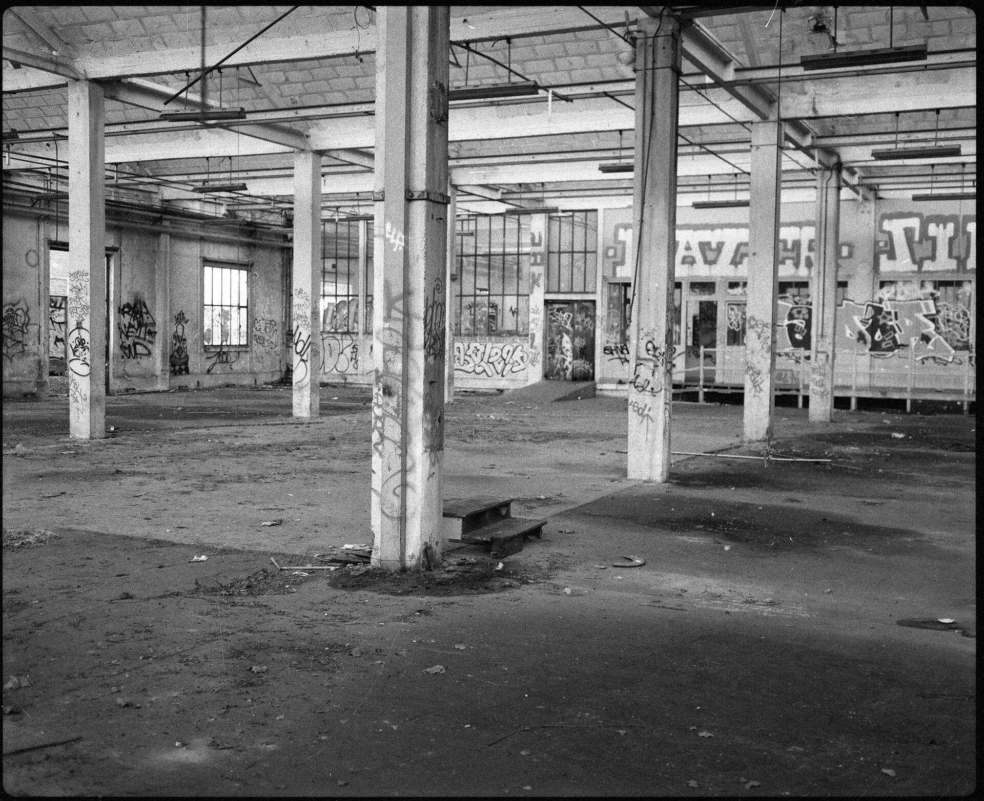 An empty industrial hall with rows of concrete pillars and graffiti on the far wall
