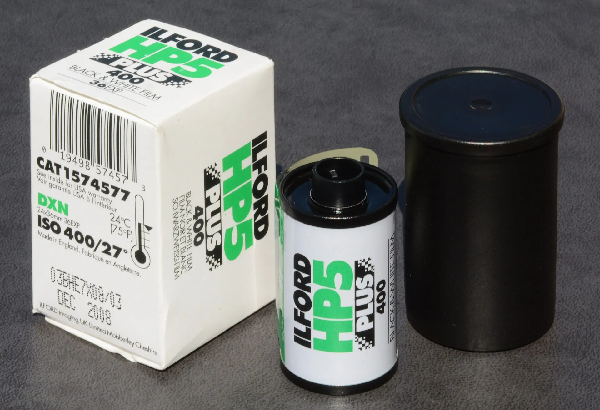 A 35mm cassette of Ilford HP5 Plus 400 next to its white and green box and a black film canister