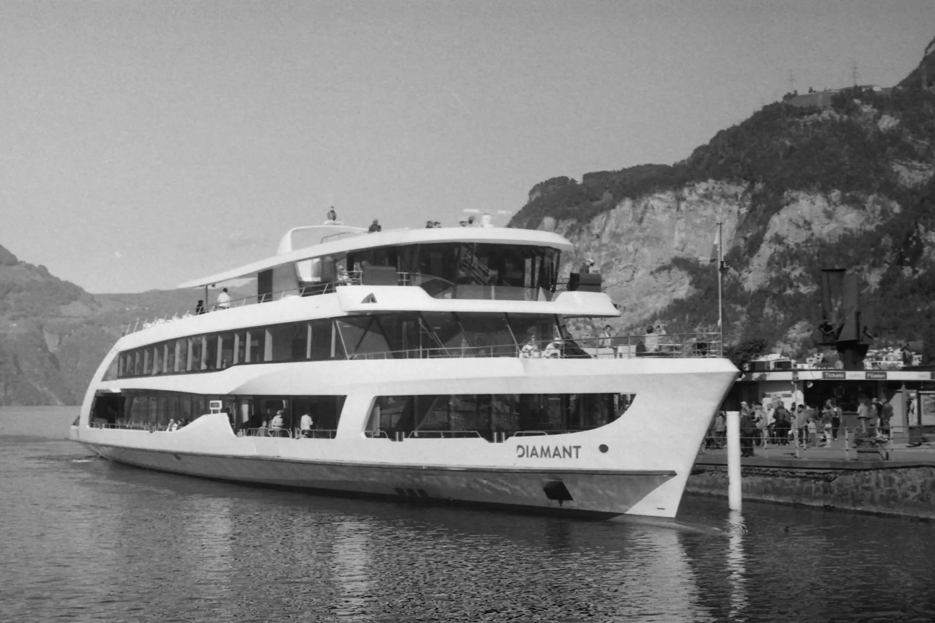 The white passenger ship MS Diamant moored at a lake pier below steep wooded mountains