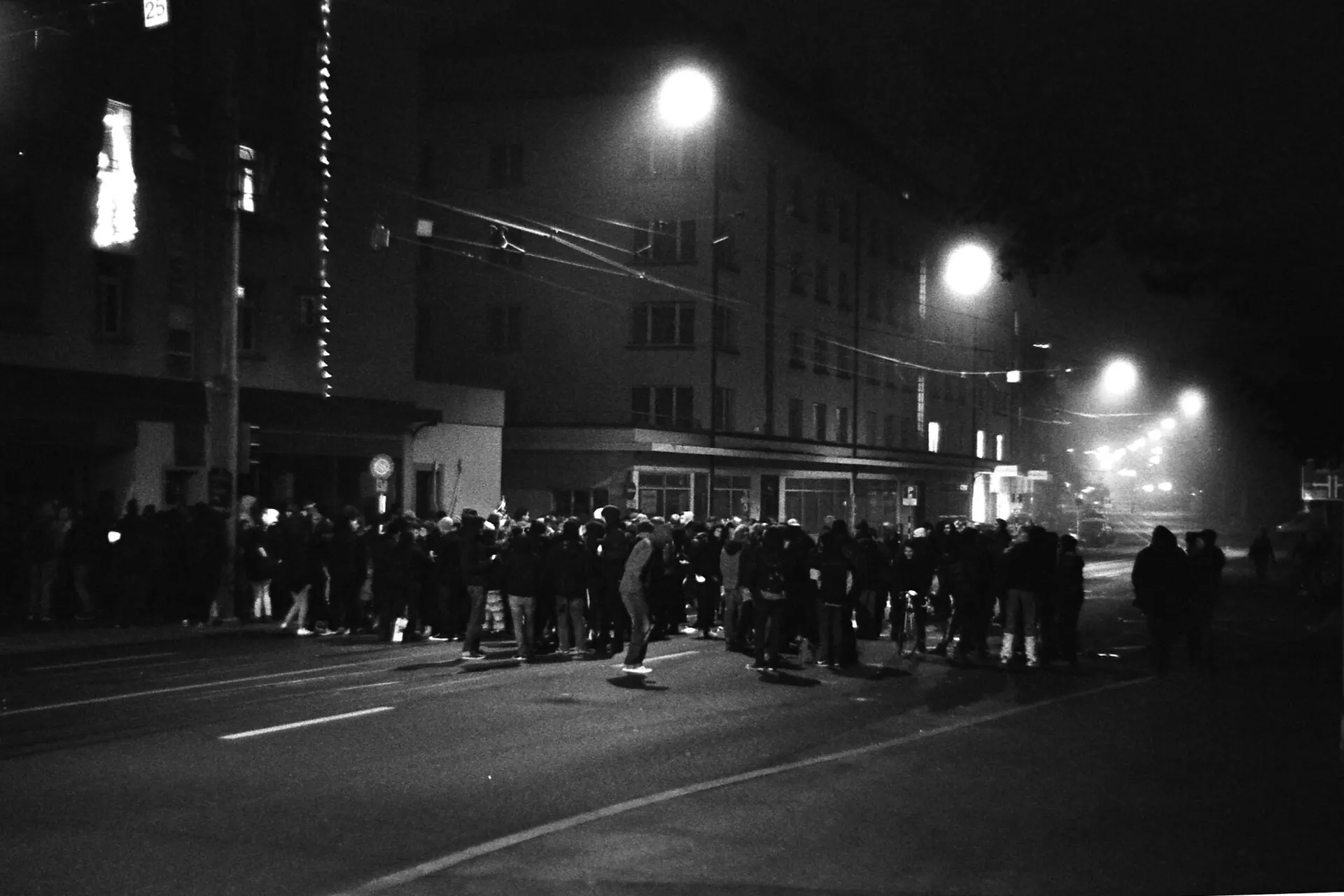 A crowd gathered in a dark street at night under streetlights