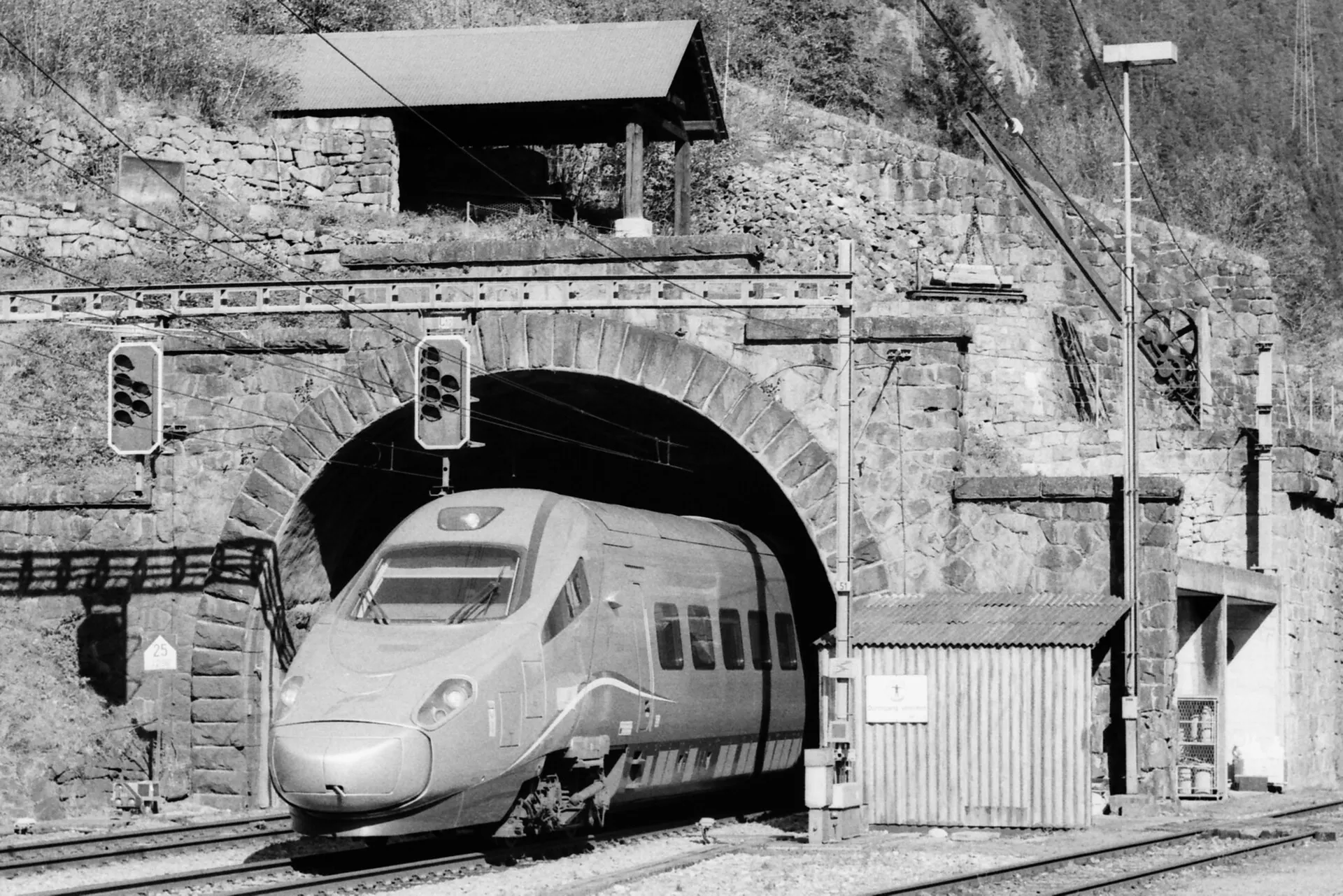 A high-speed train leaving a stone tunnel portal into a station