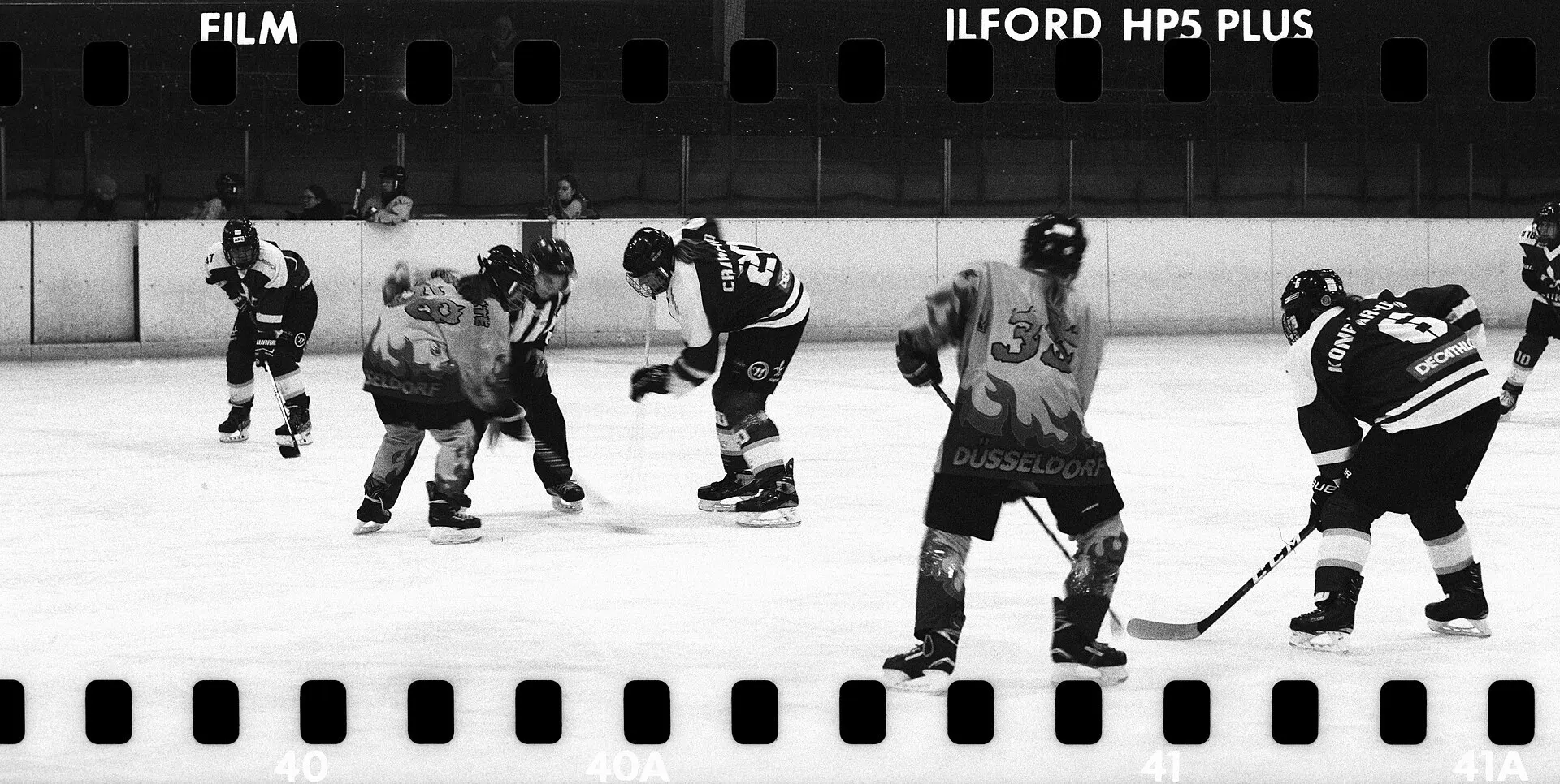 A women’s ice hockey faceoff seen from the stands, with the film rebate visible