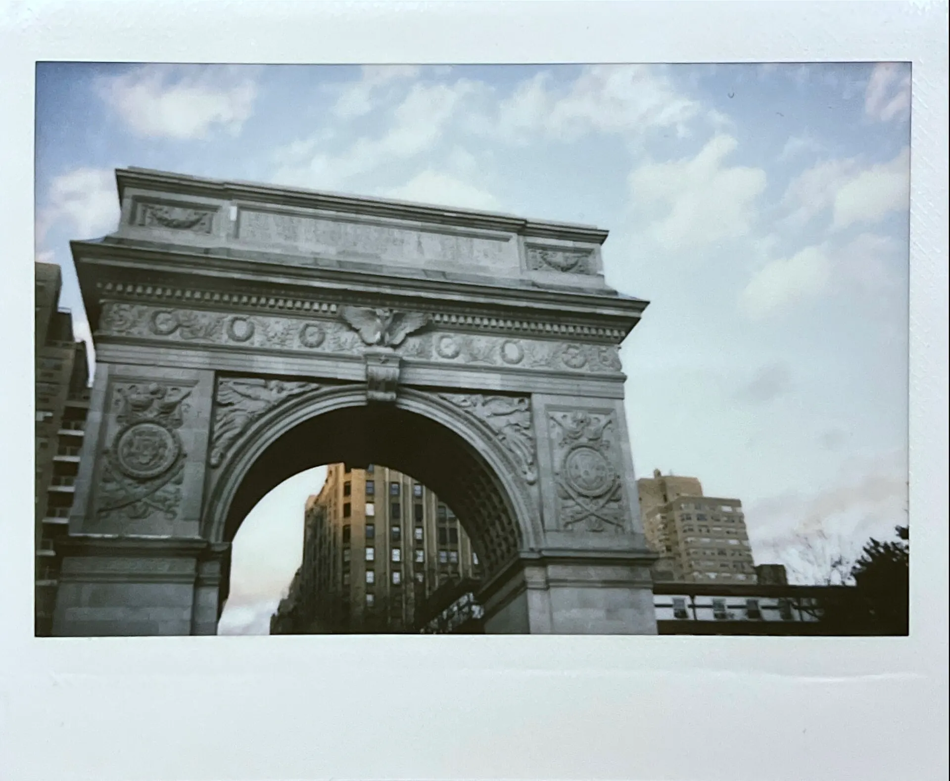 Instax Wide print of the Washington Square Arch in New York under a blue sky with clouds, in a white frame
