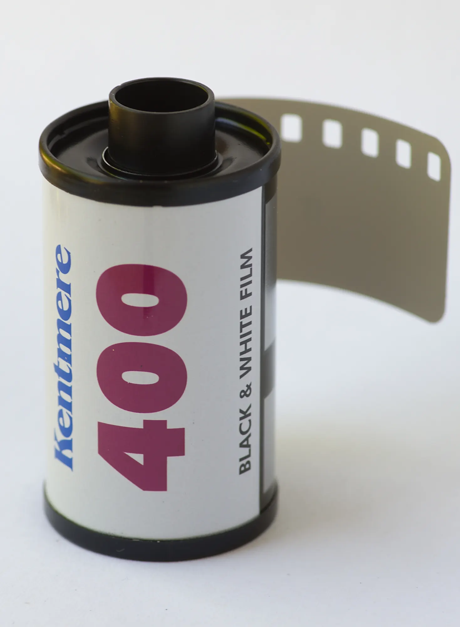 A 35mm cassette of Kentmere 400 black and white film with the film leader pulled out, on a plain white background