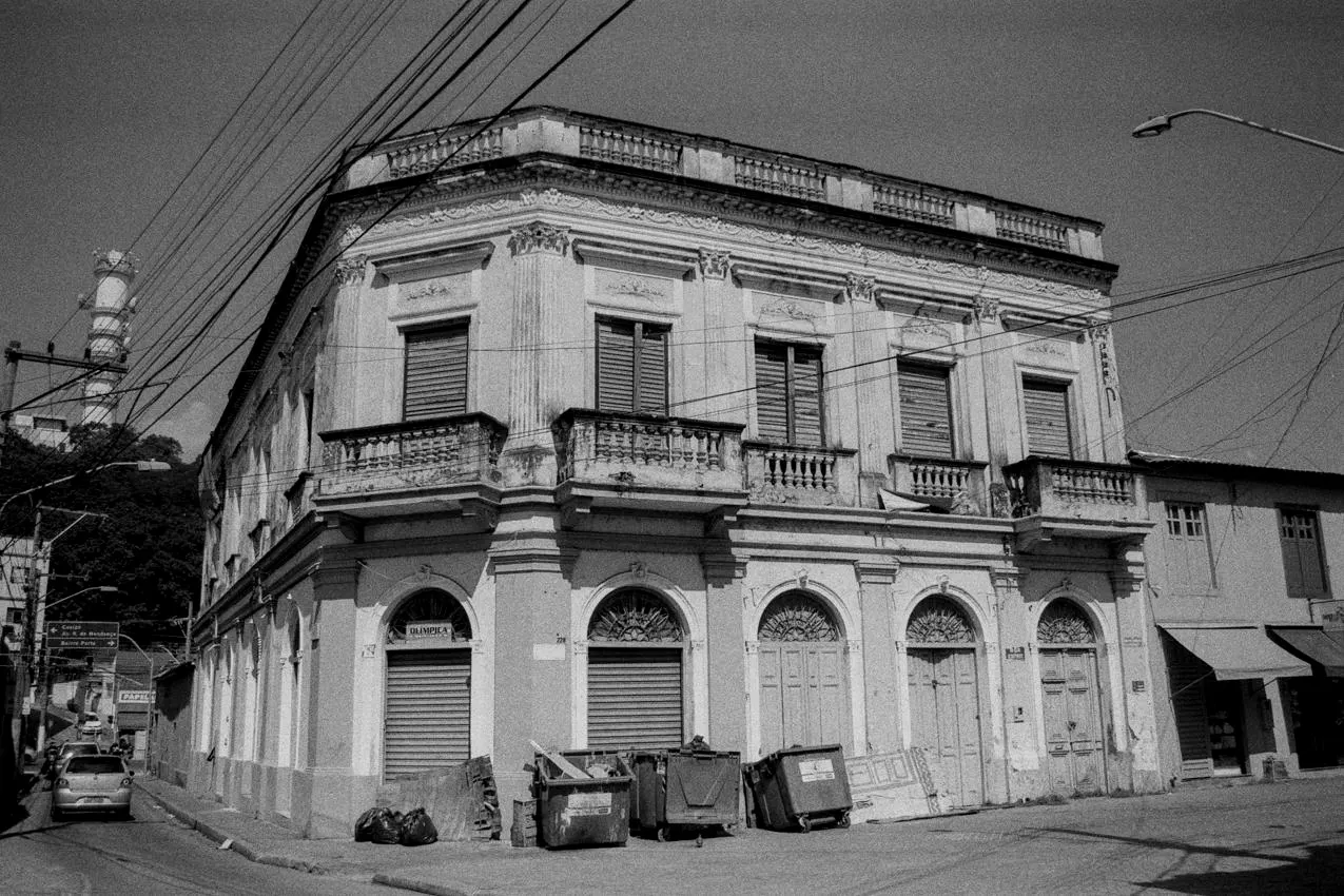 Black and white photo of an old two-story corner building with balconies and arched doors on a street