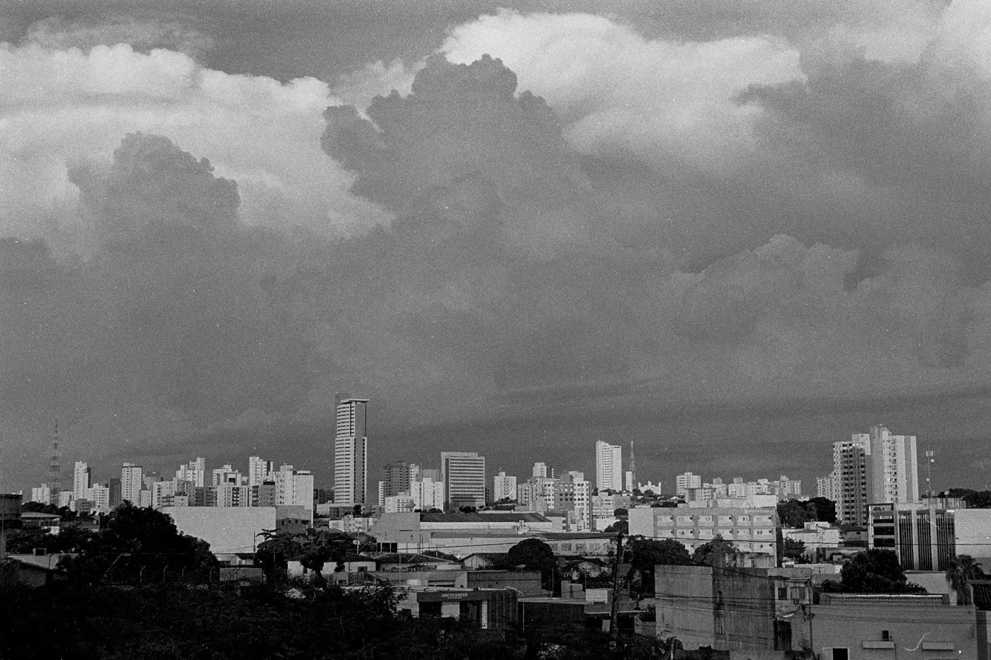 Black and white photo of a city skyline under large bright cumulus clouds