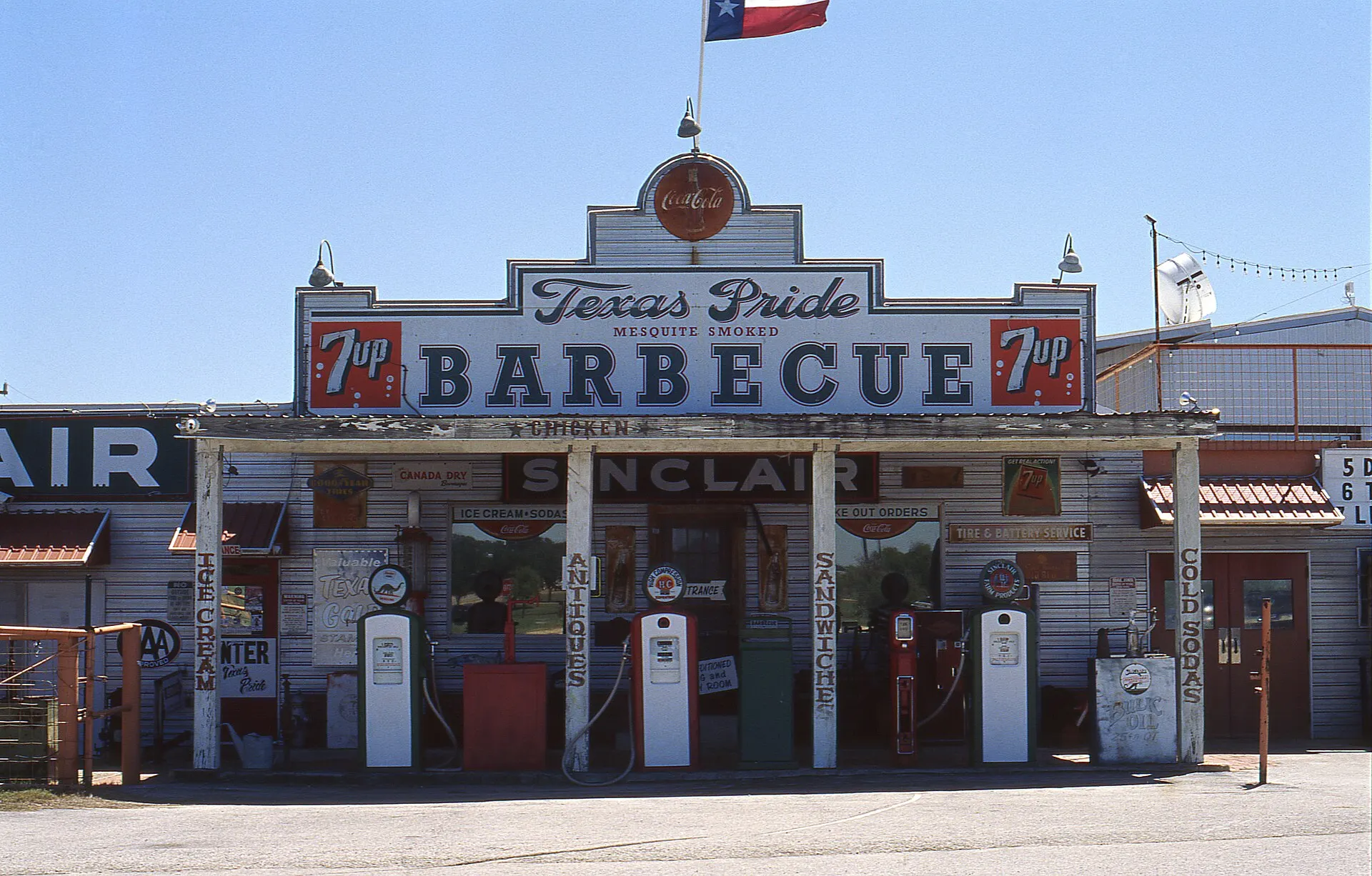 Front of Texas Pride Barbecue, a roadside restaurant with old gas pumps, under a clear blue sky