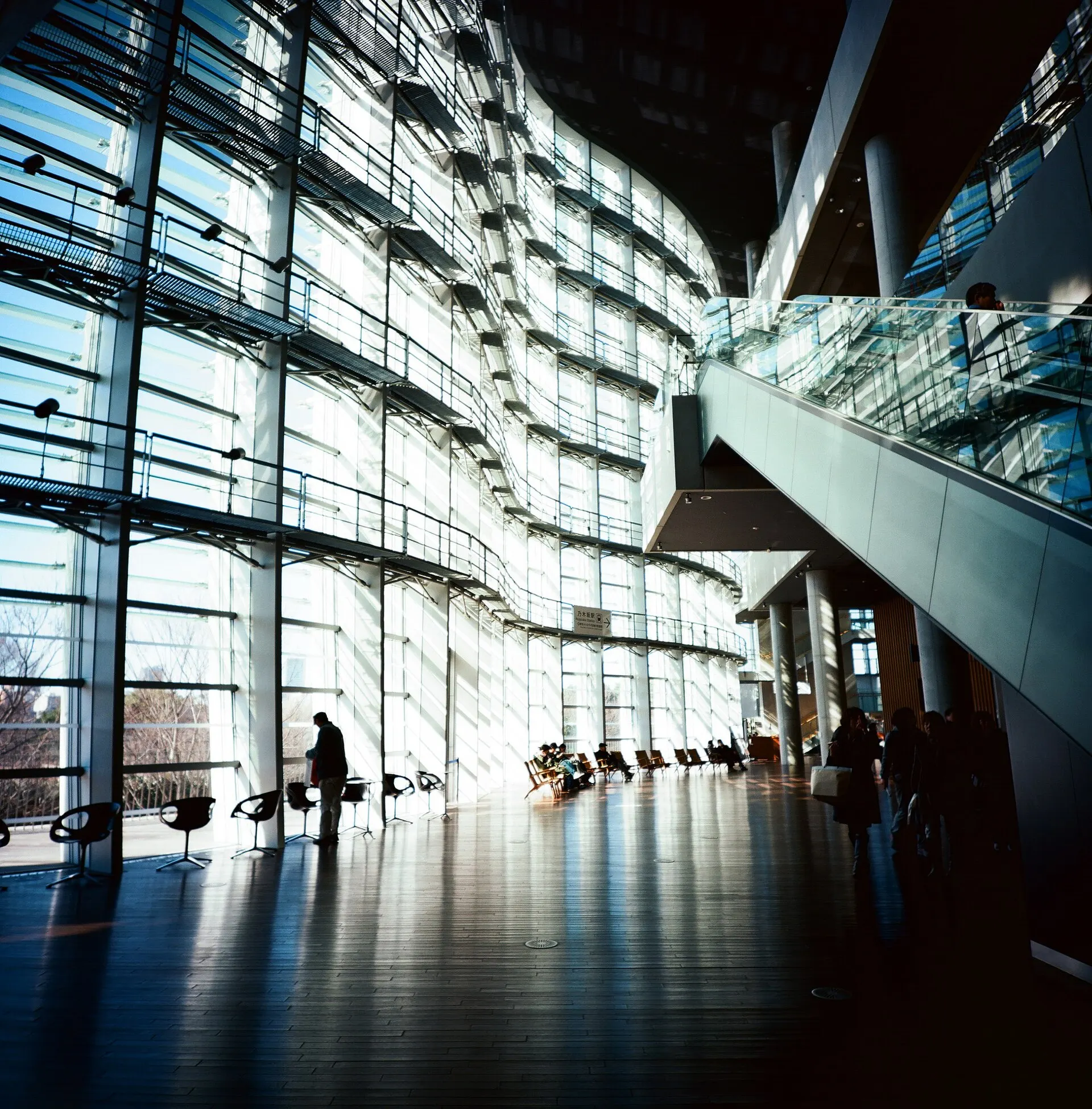 The curved glass facade of a museum seen from inside, with a few small figures in the lobby