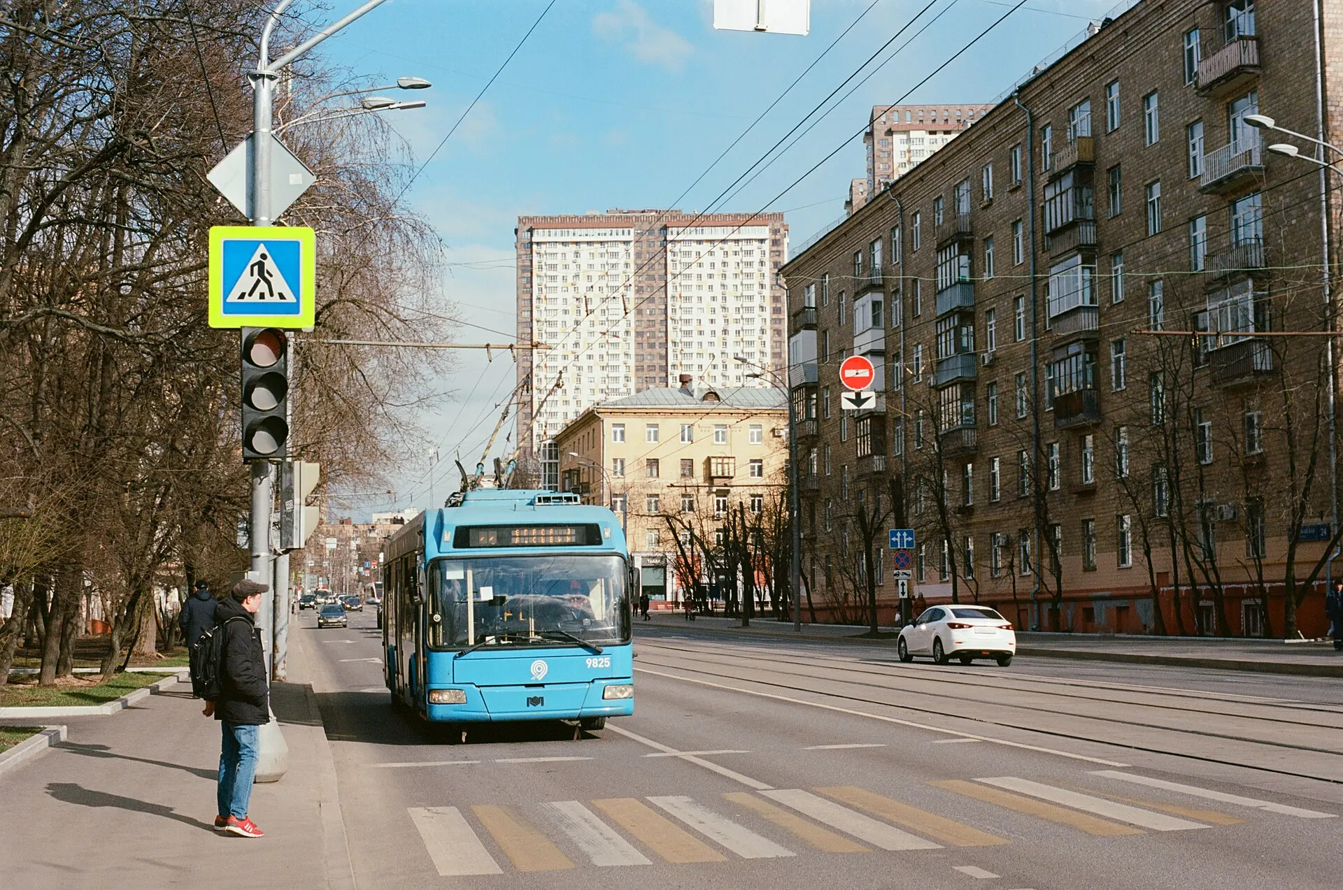 A blue trolleybus at a crosswalk on a wide street lined with apartment blocks