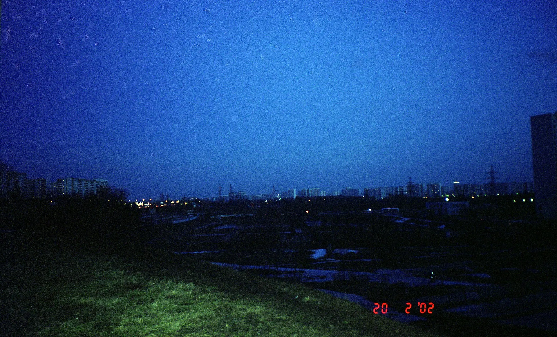 City skyline at dusk under a deep blue sky with a few lights and a date stamp