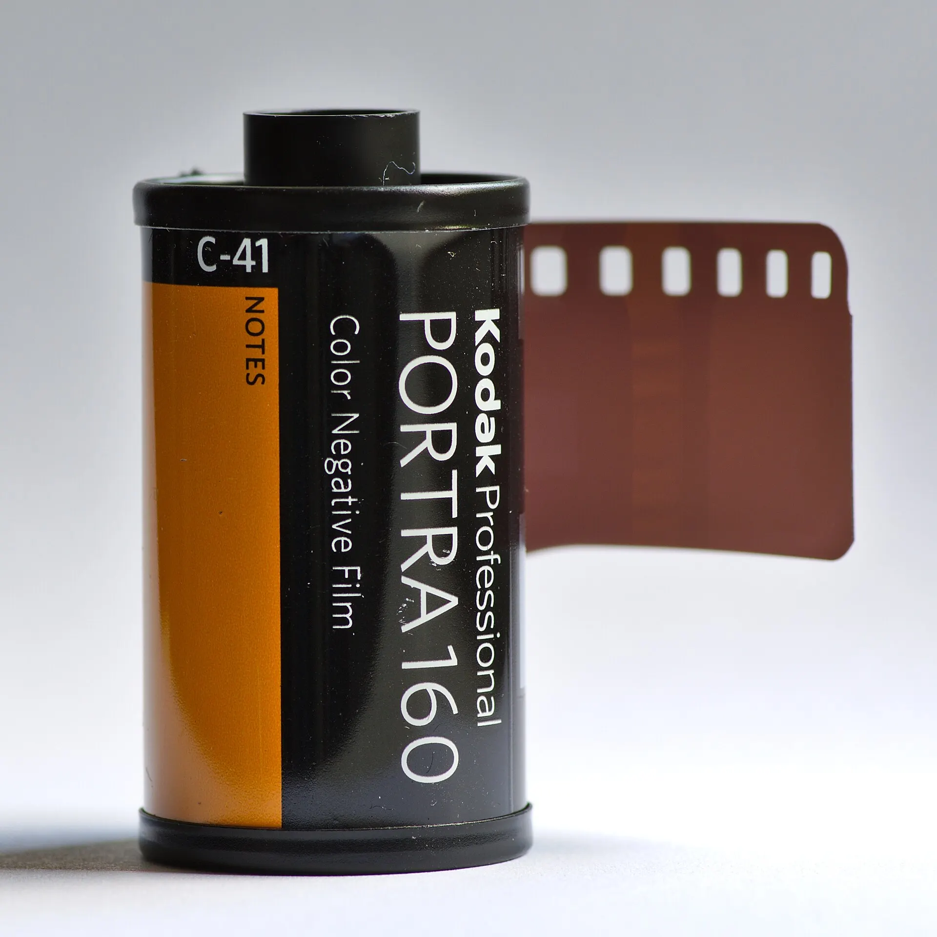 A 35mm cartridge of Kodak Professional Portra 160 color negative film with the leader pulled out, on a plain white background
