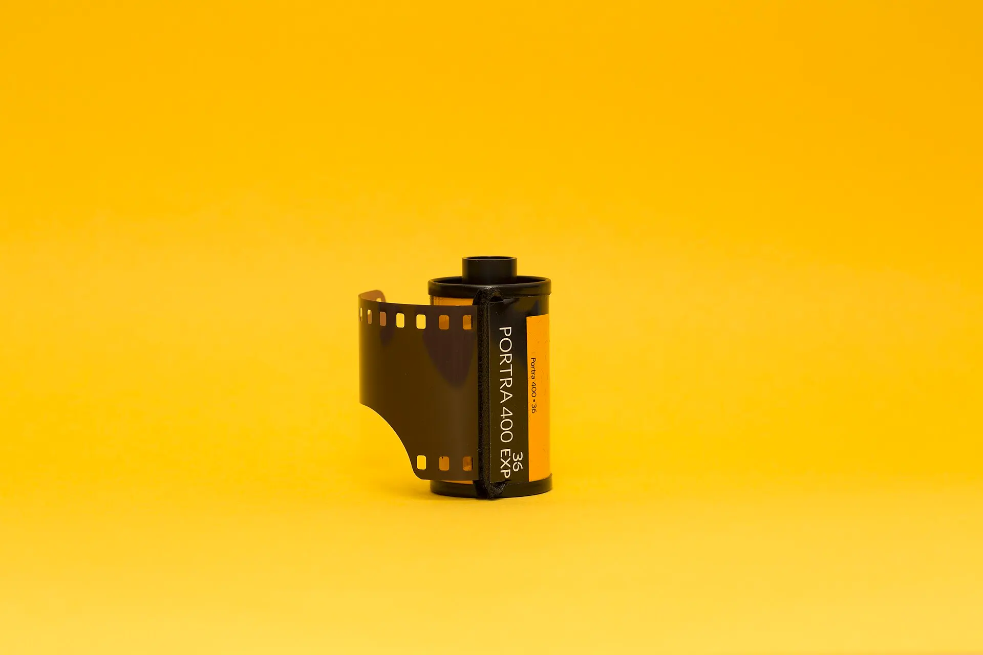 A 36-exposure 35mm cassette of Kodak Portra 400 with the film leader pulled out, on a plain yellow background