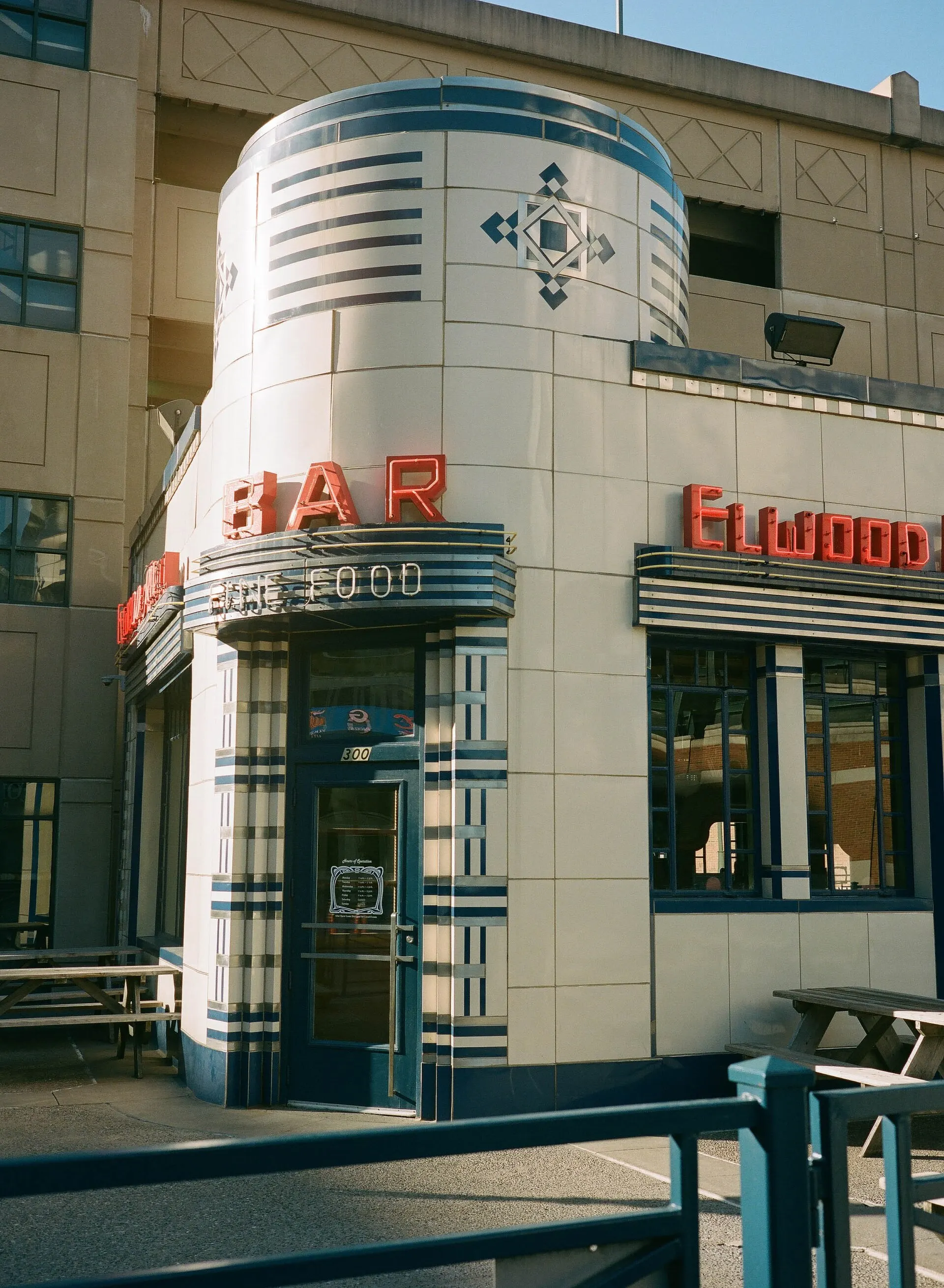 A rounded Art Deco storefront with cream and teal tiles and red lettering under a blue sky