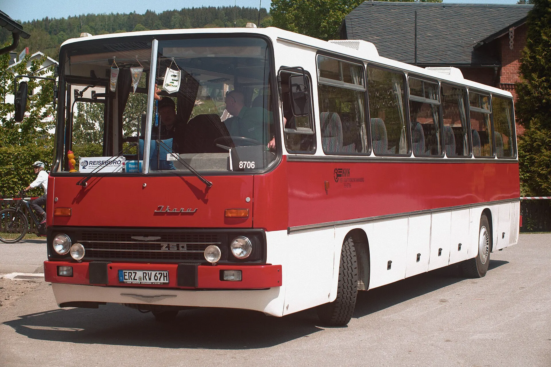 Front of a red and white Ikarus 250 coach parked at a small station on a sunny day
