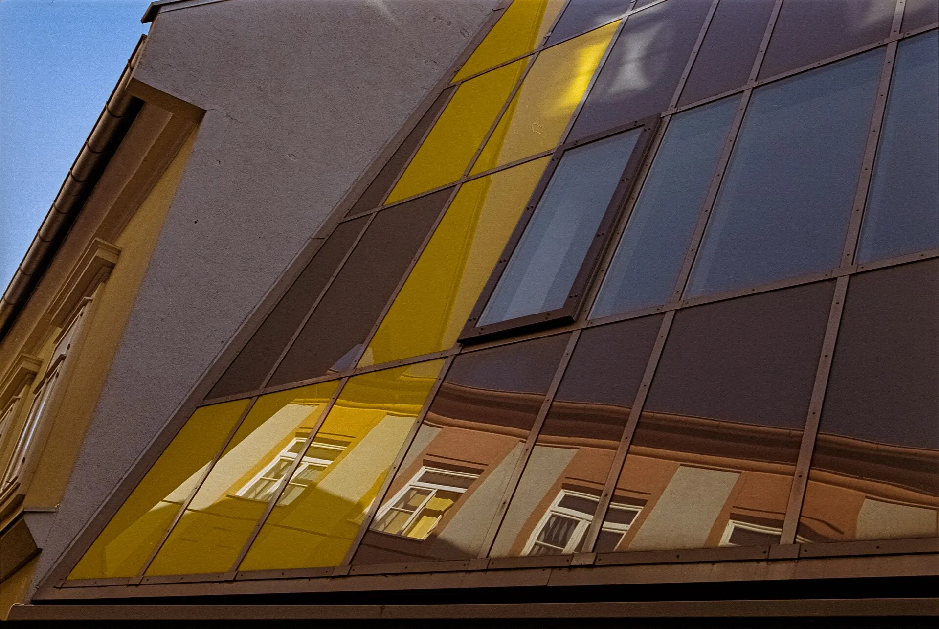 A building facade with yellow and gray glass panels, seen from below at an angle