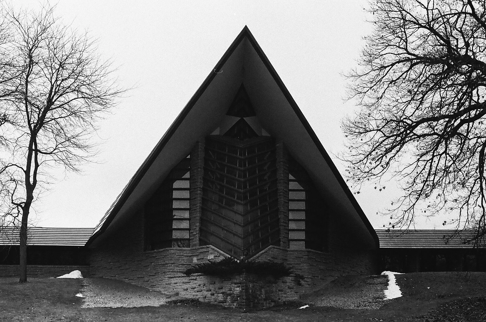 Steep triangular roof and stone walls of a church framed by bare winter trees