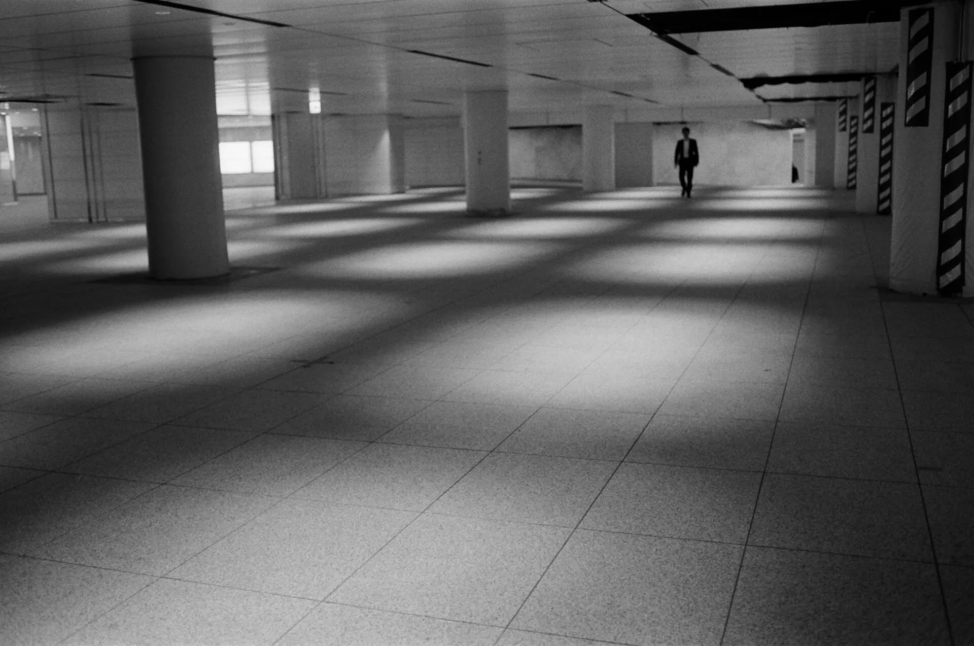 Long underground walkway with pools of light on the floor and one distant person