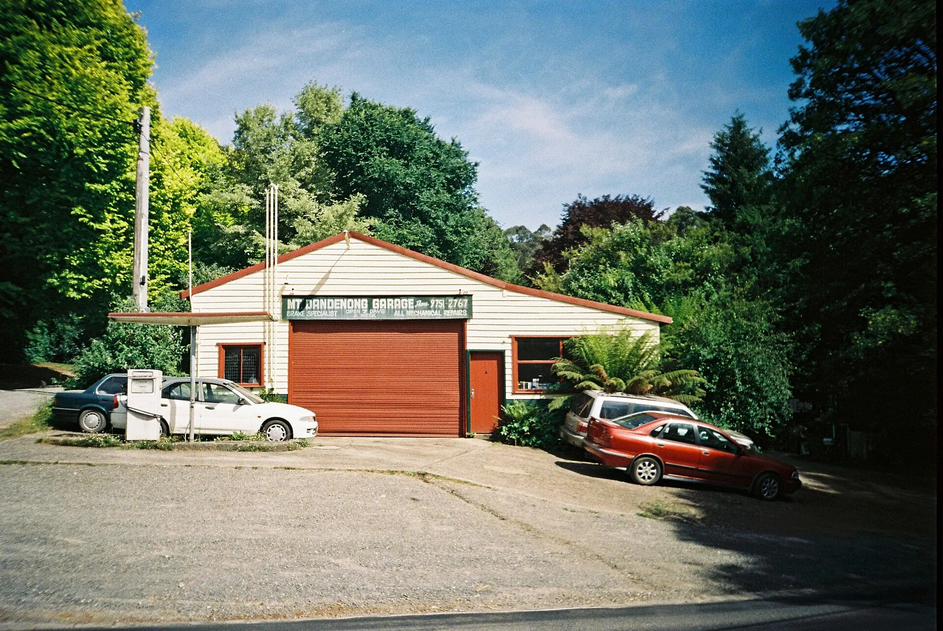 A red garage door and parked cars under green trees on a sunny day