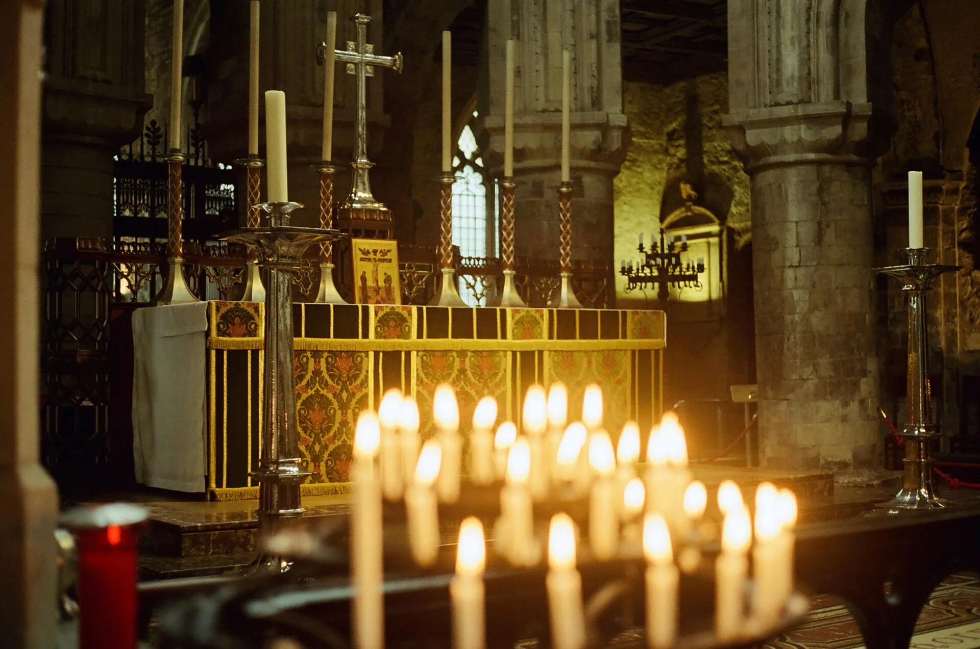 Rows of lit candles in front of a carved altar inside a dim stone church