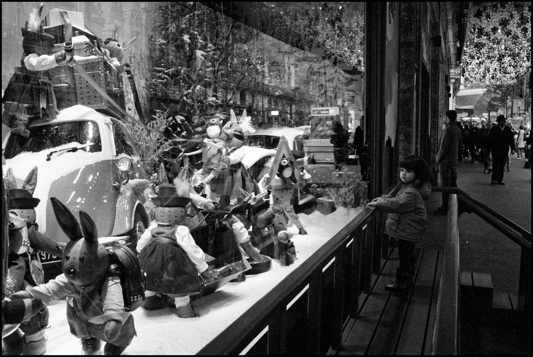 Black and white photo of a Christmas shop window full of toys along a city sidewalk