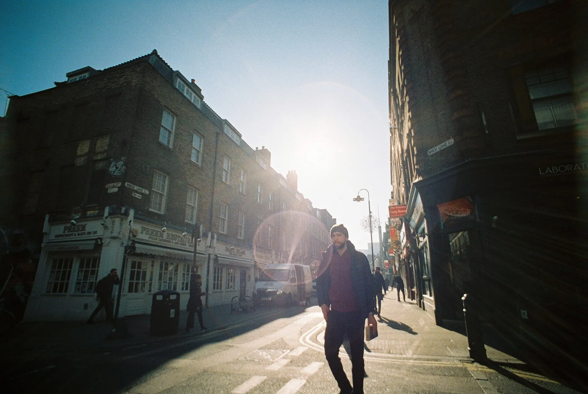 Low morning sun shining down a London street lined with brick buildings, a walker in silhouette