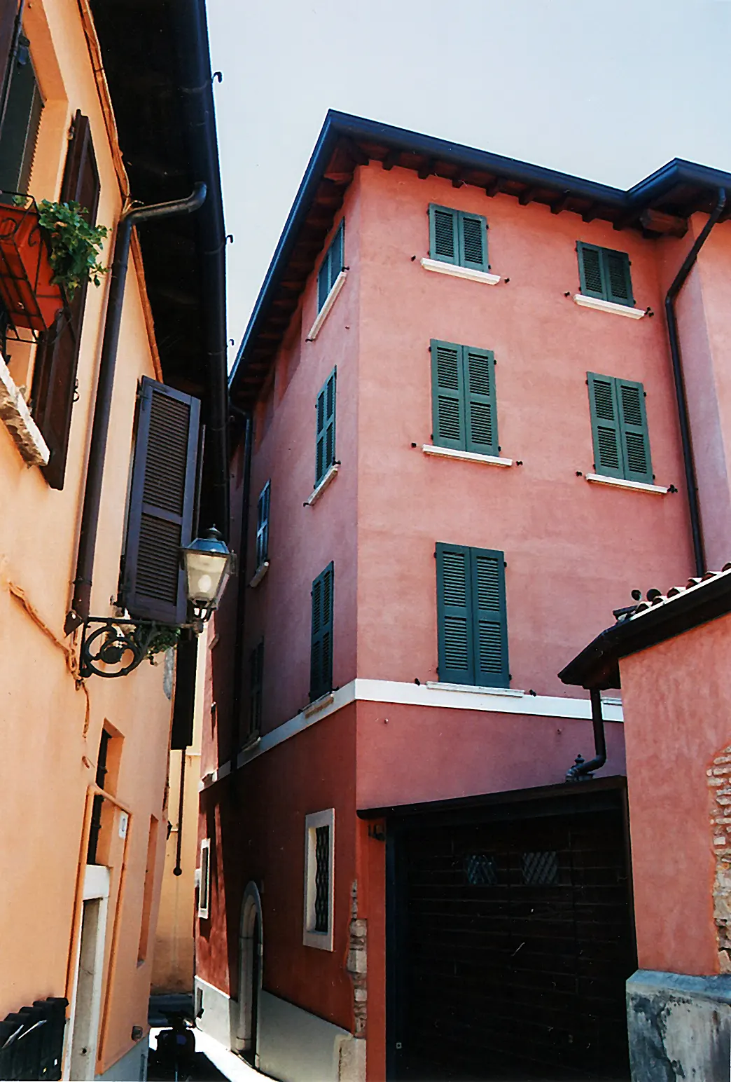 A narrow alley between orange and red buildings with green shutters