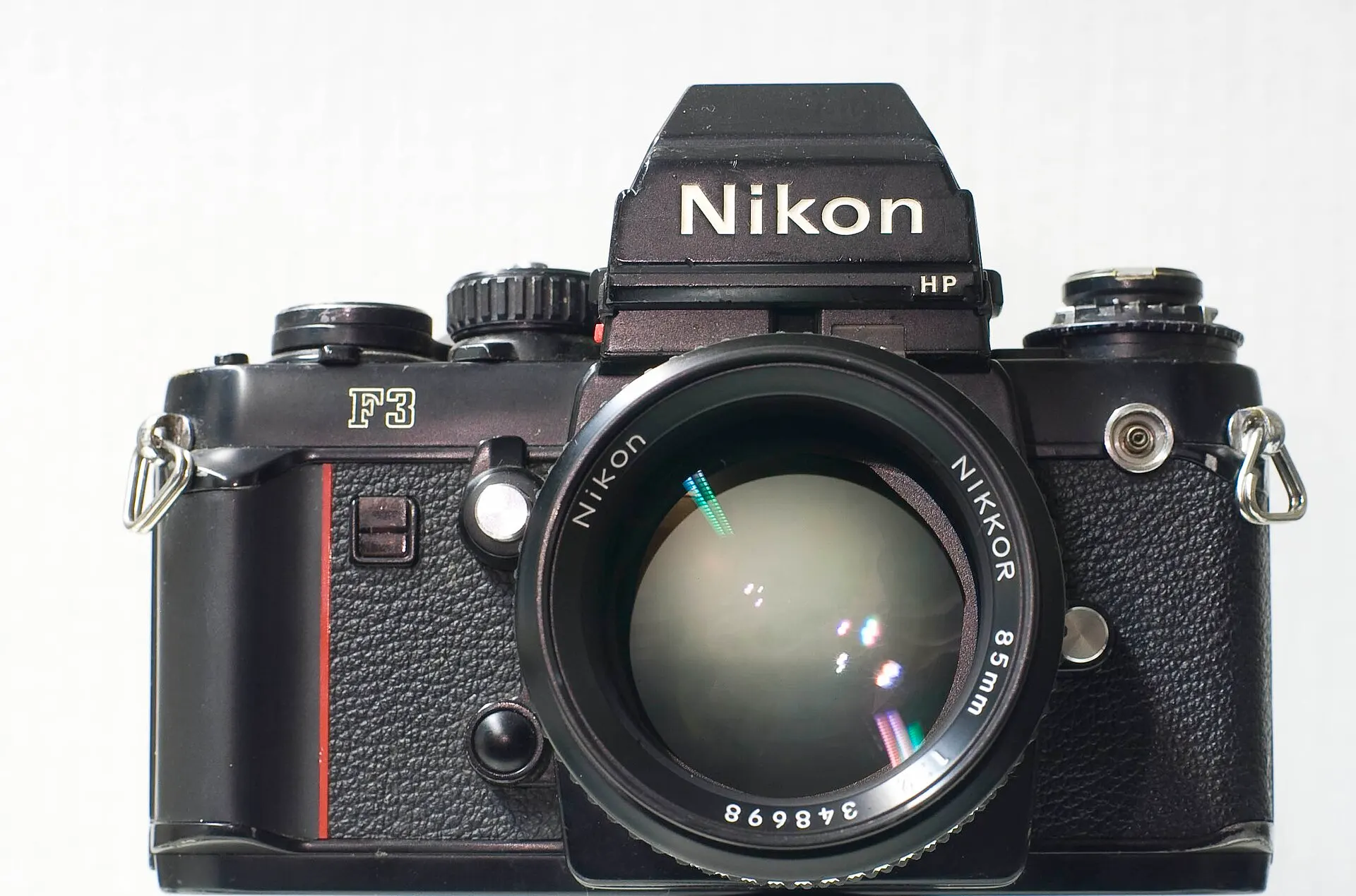 Black Nikon F3 HP with the high-eyepoint finder and an AI-S Nikkor 85mm f/2 lens, front view on a white background