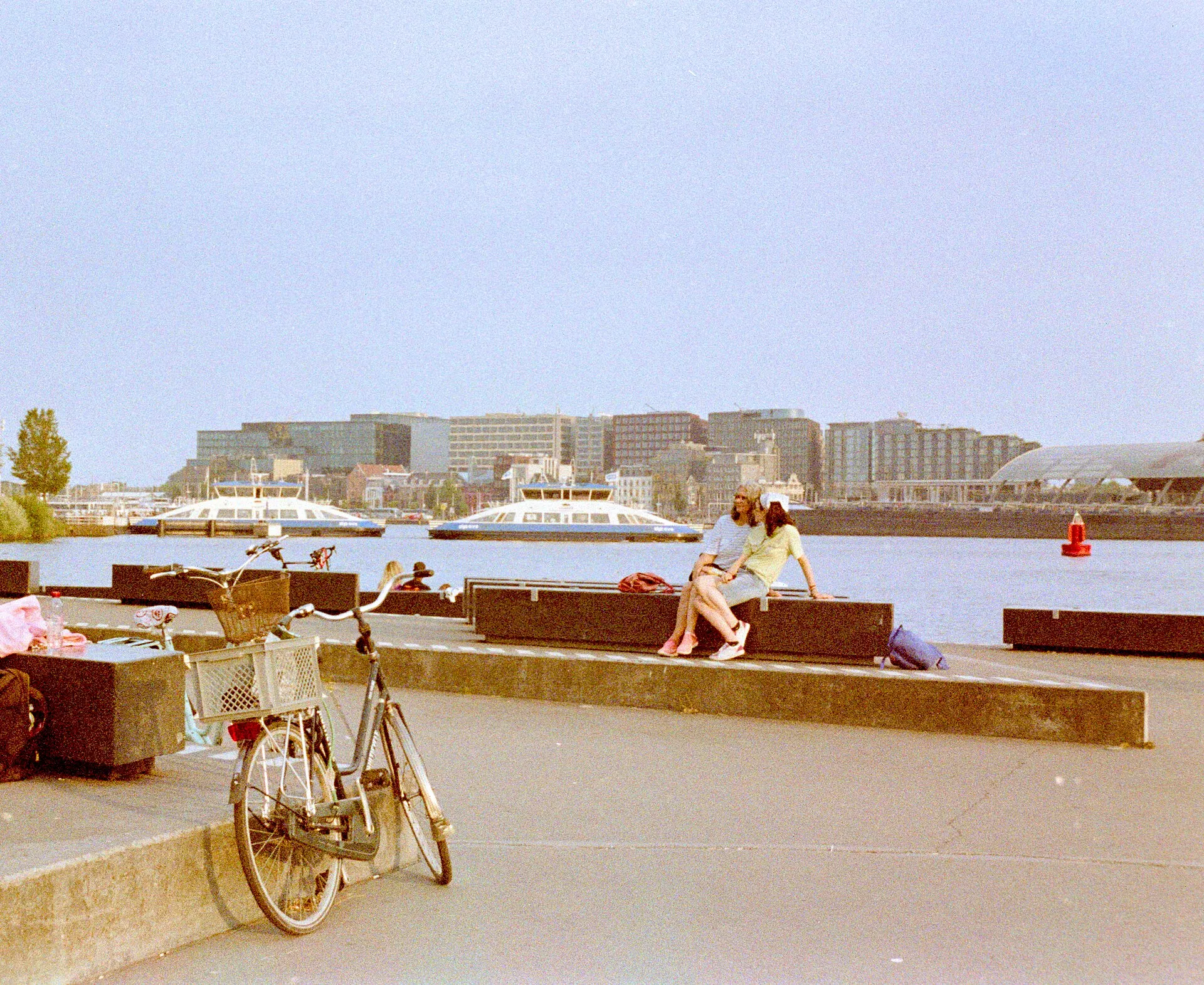 A waterfront promenade with a parked bicycle and people sitting by the water