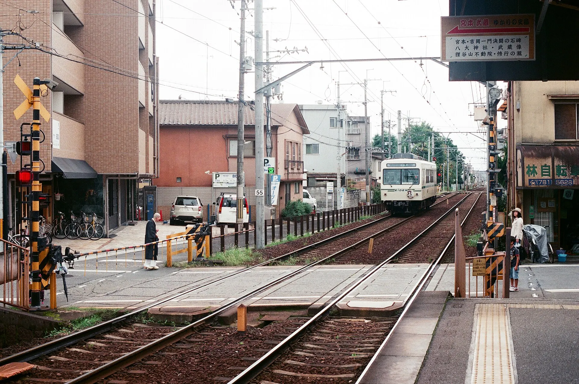 Small two-car train arriving at a level crossing beside a station platform in a residential street