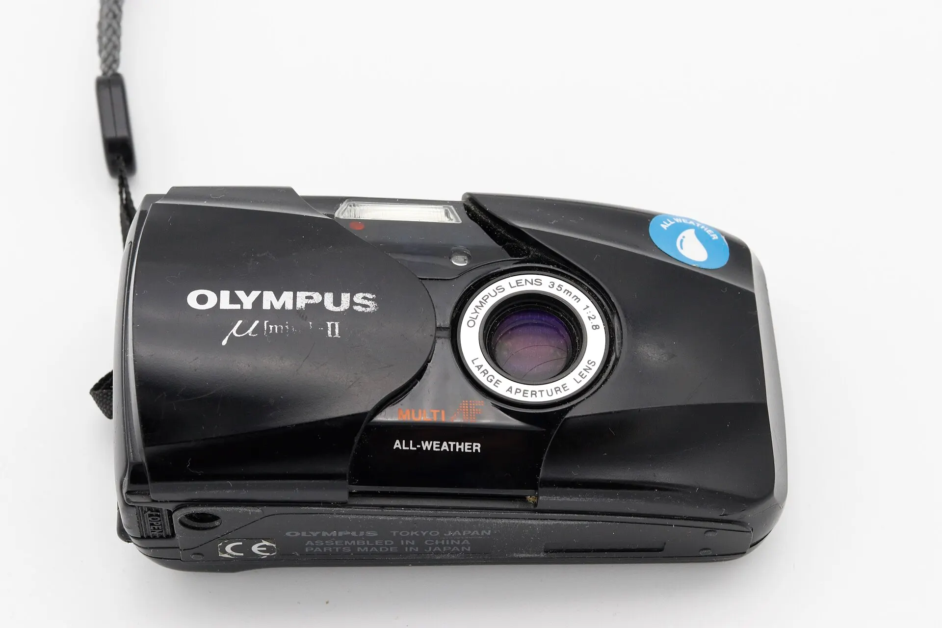 Black Olympus Mju II (Stylus Epic) seen from the front with its sliding lens cover open, on a white background