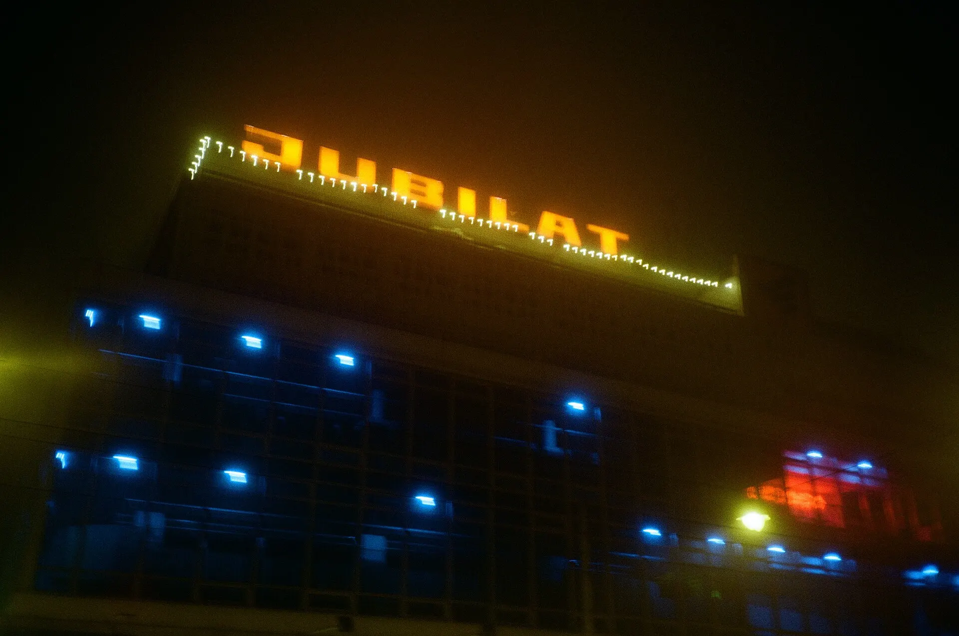 Lit-up Jubilat sign and blue windows on a building at night