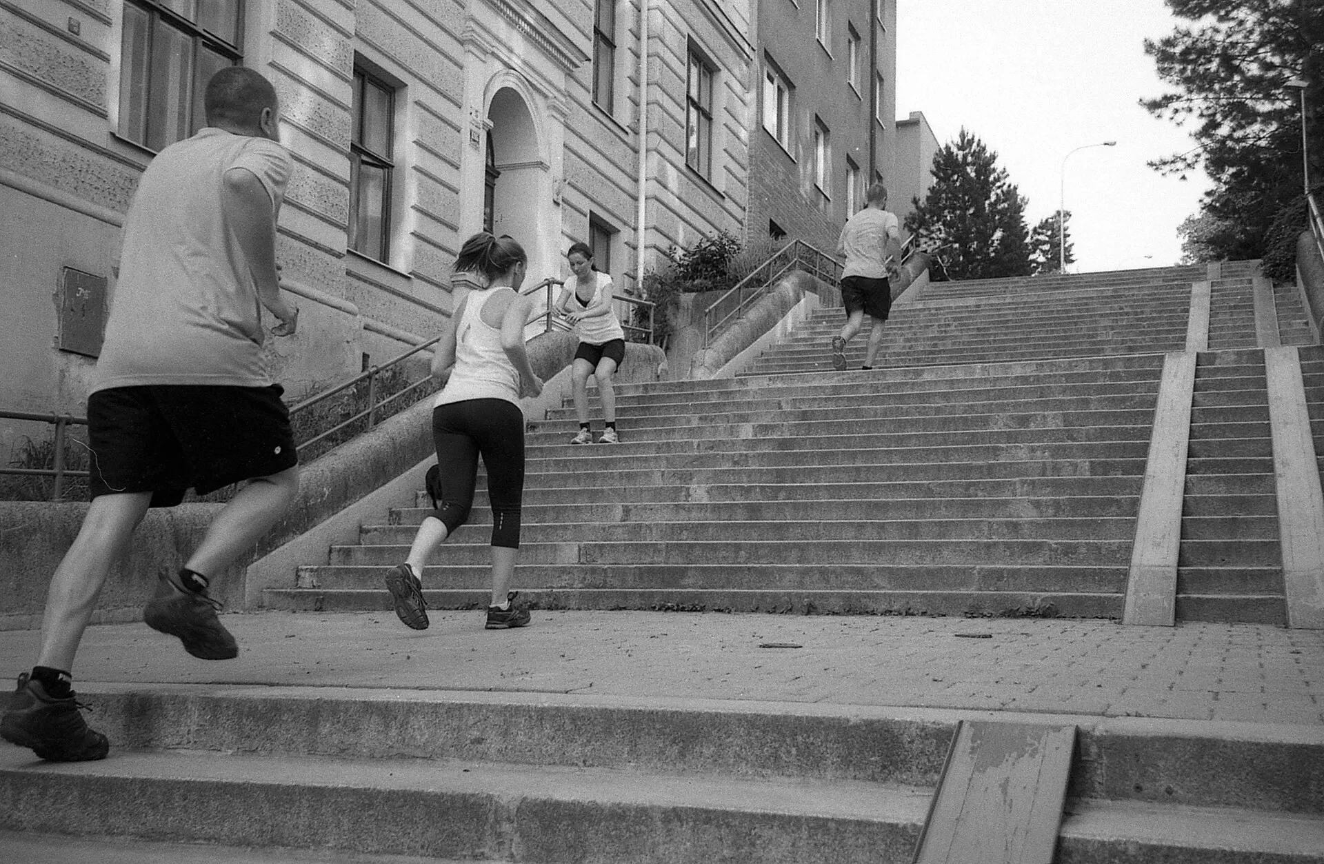 Black and white photo of people running up a long flight of outdoor stairs, seen from behind