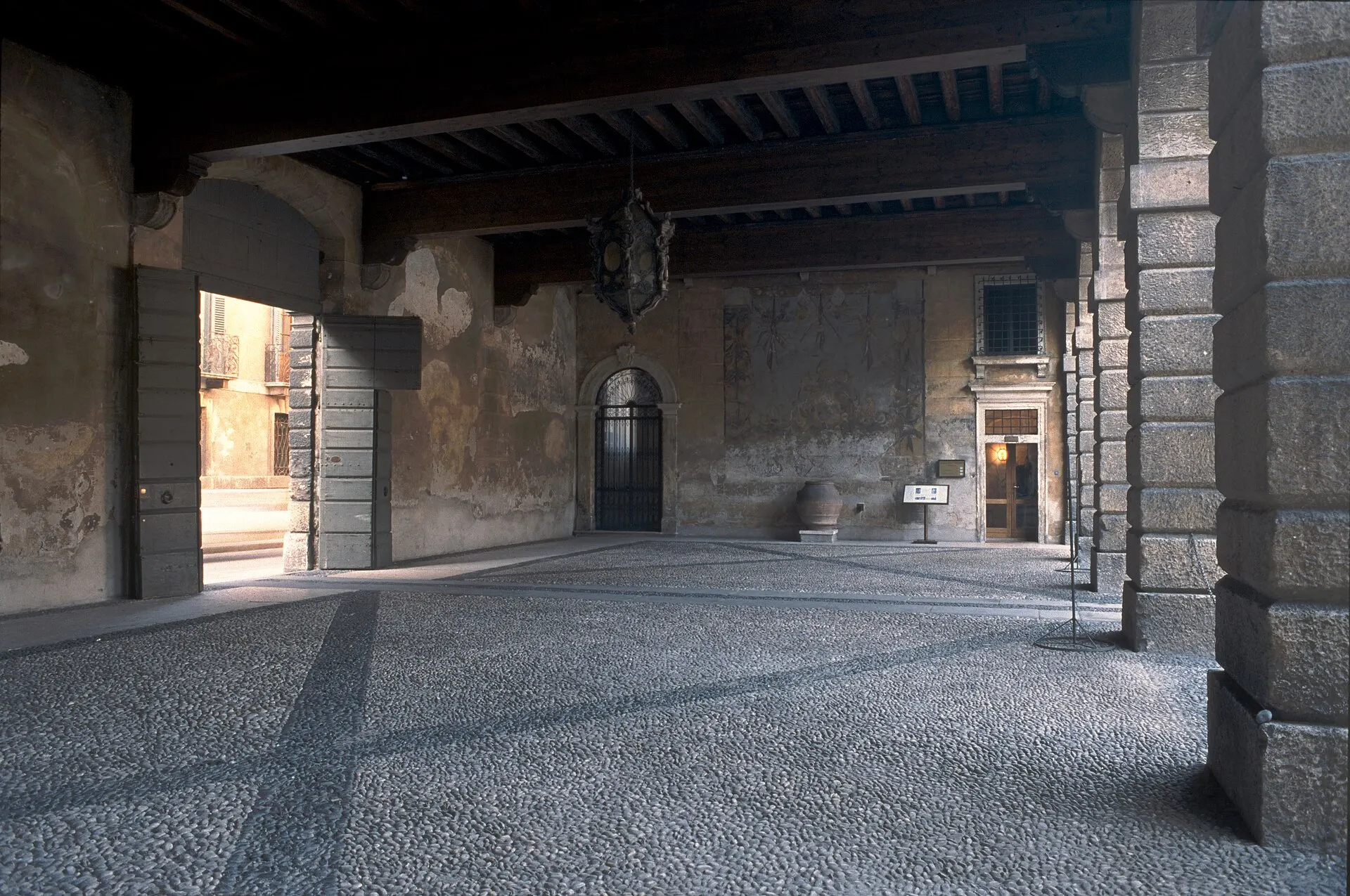 Covered portico with wooden ceiling beams, stone pillars and a patterned stone floor