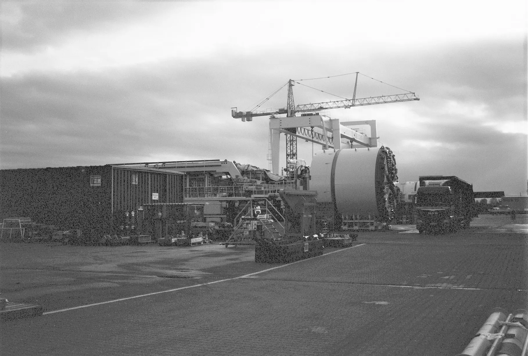 Black and white industrial yard with a crane and large machinery at dusk