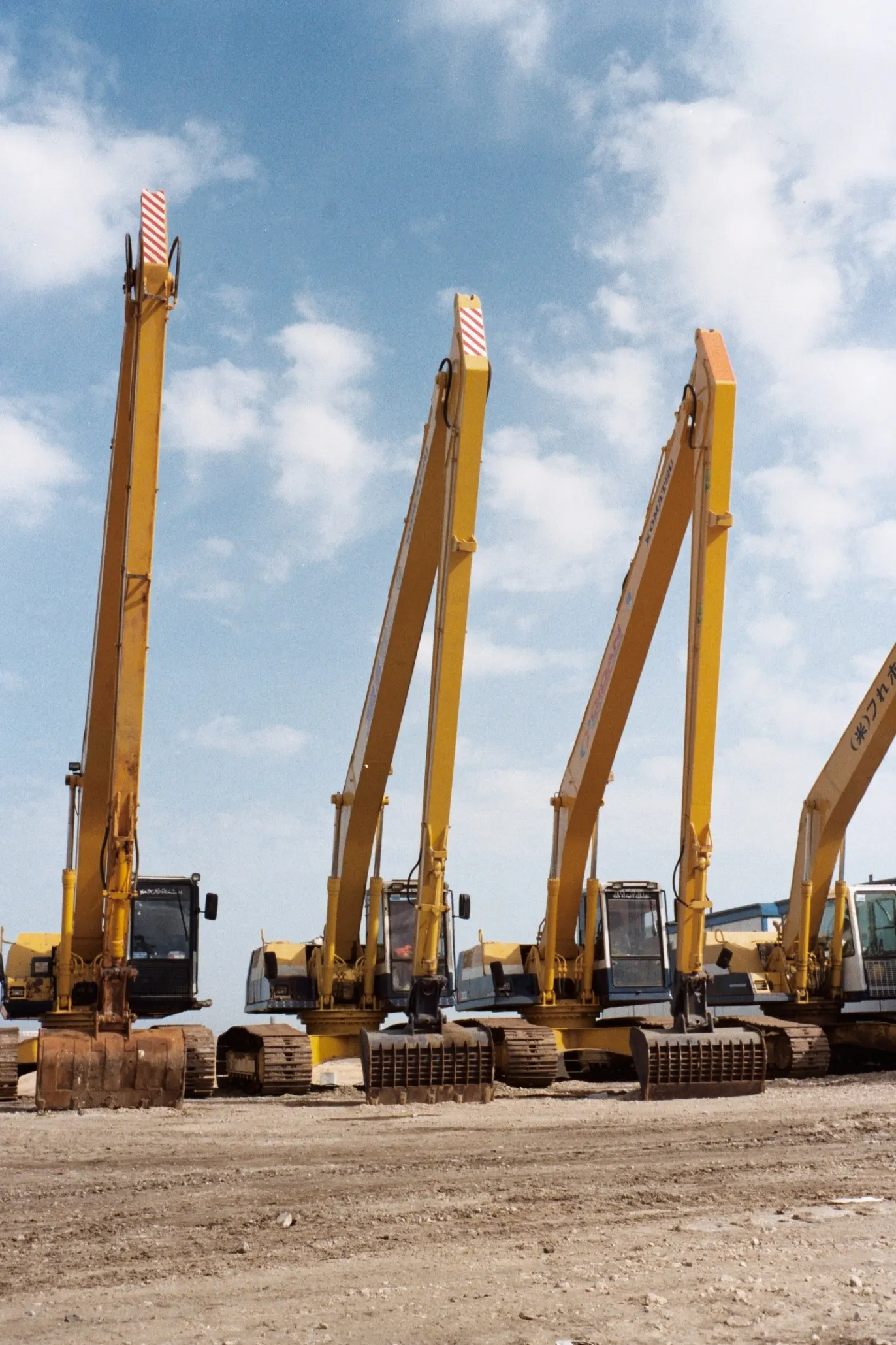 Row of yellow long-reach hydraulic excavators against a blue sky