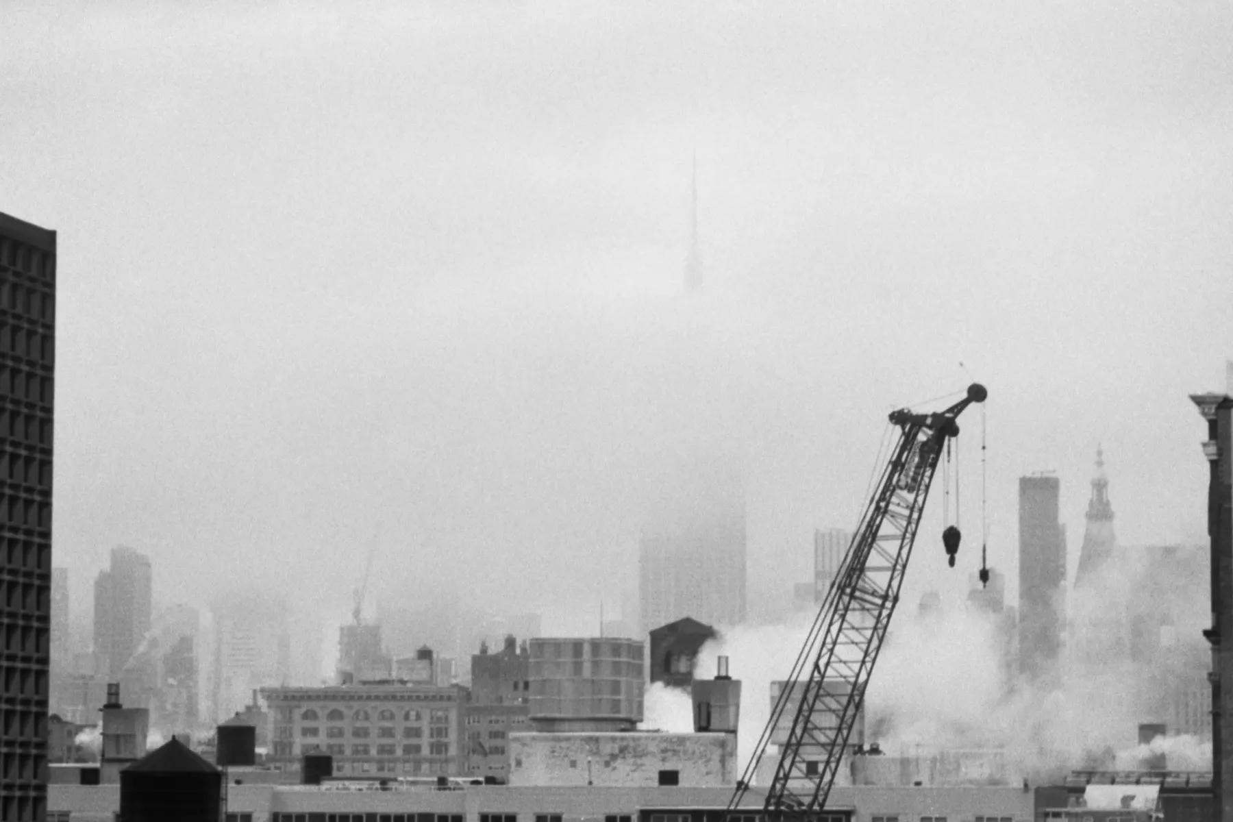 Black-and-white view of the Manhattan skyline in fog with a construction crane in the foreground