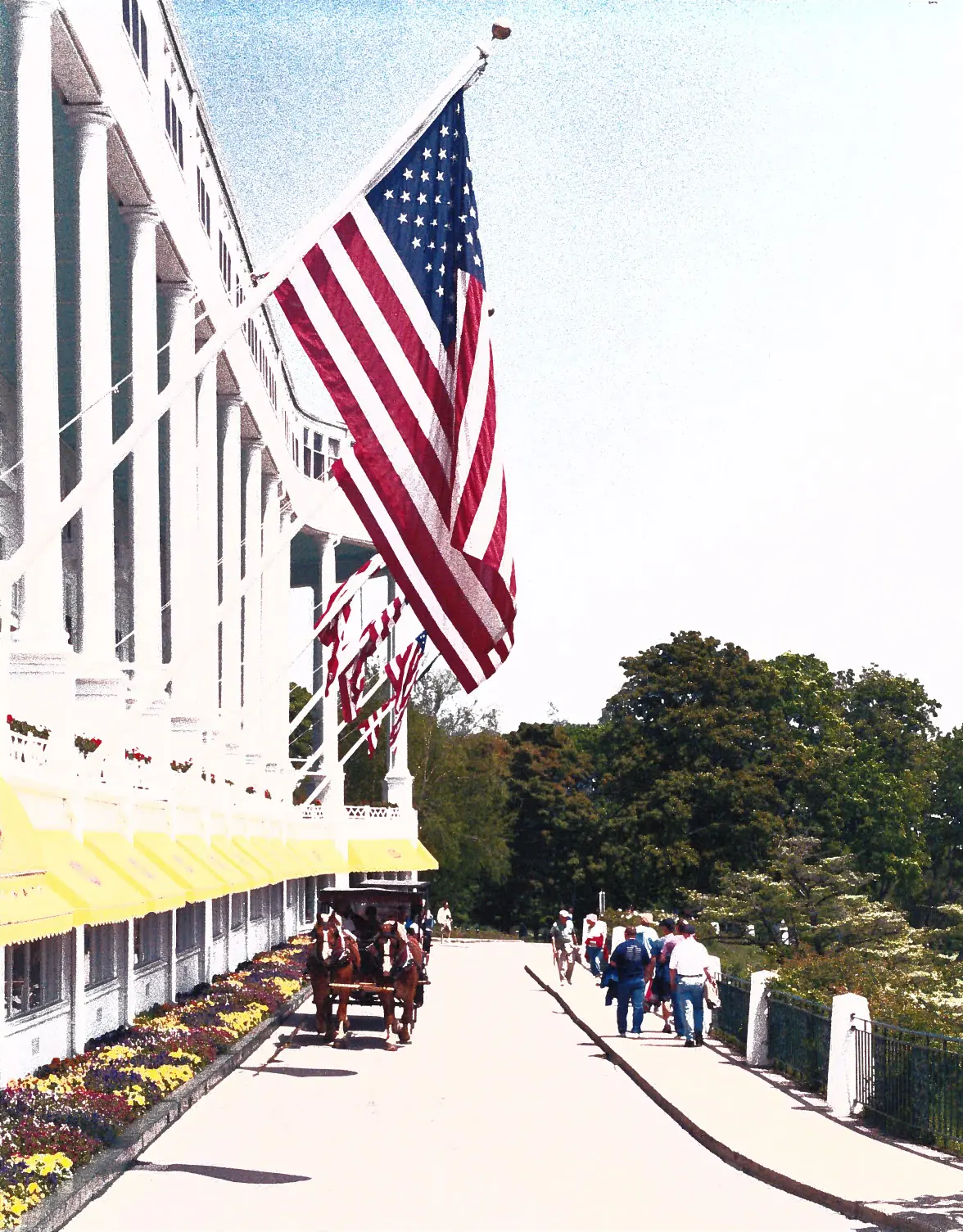American flags on the white porch of the Grand Hotel with a horse carriage on the drive