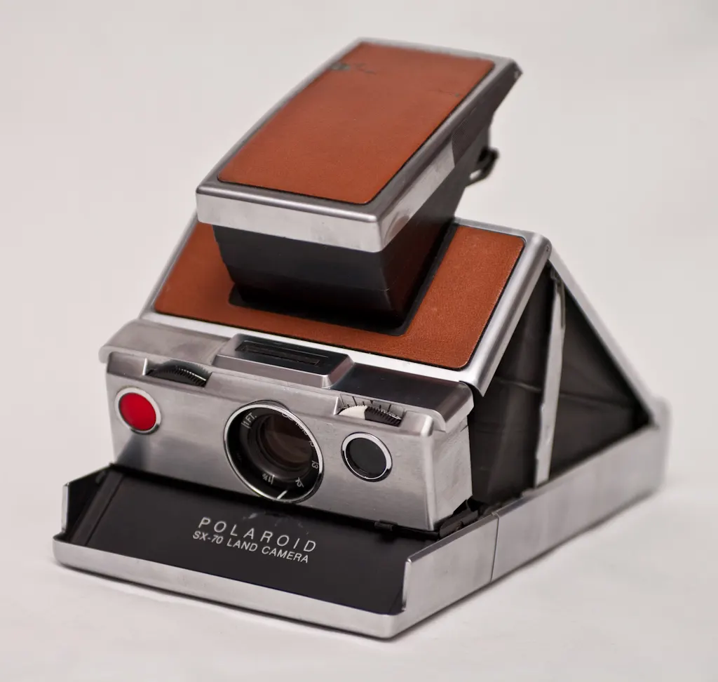 Chrome Polaroid SX-70 Land Camera with tan leather panels, unfolded and ready to shoot, on a plain white background