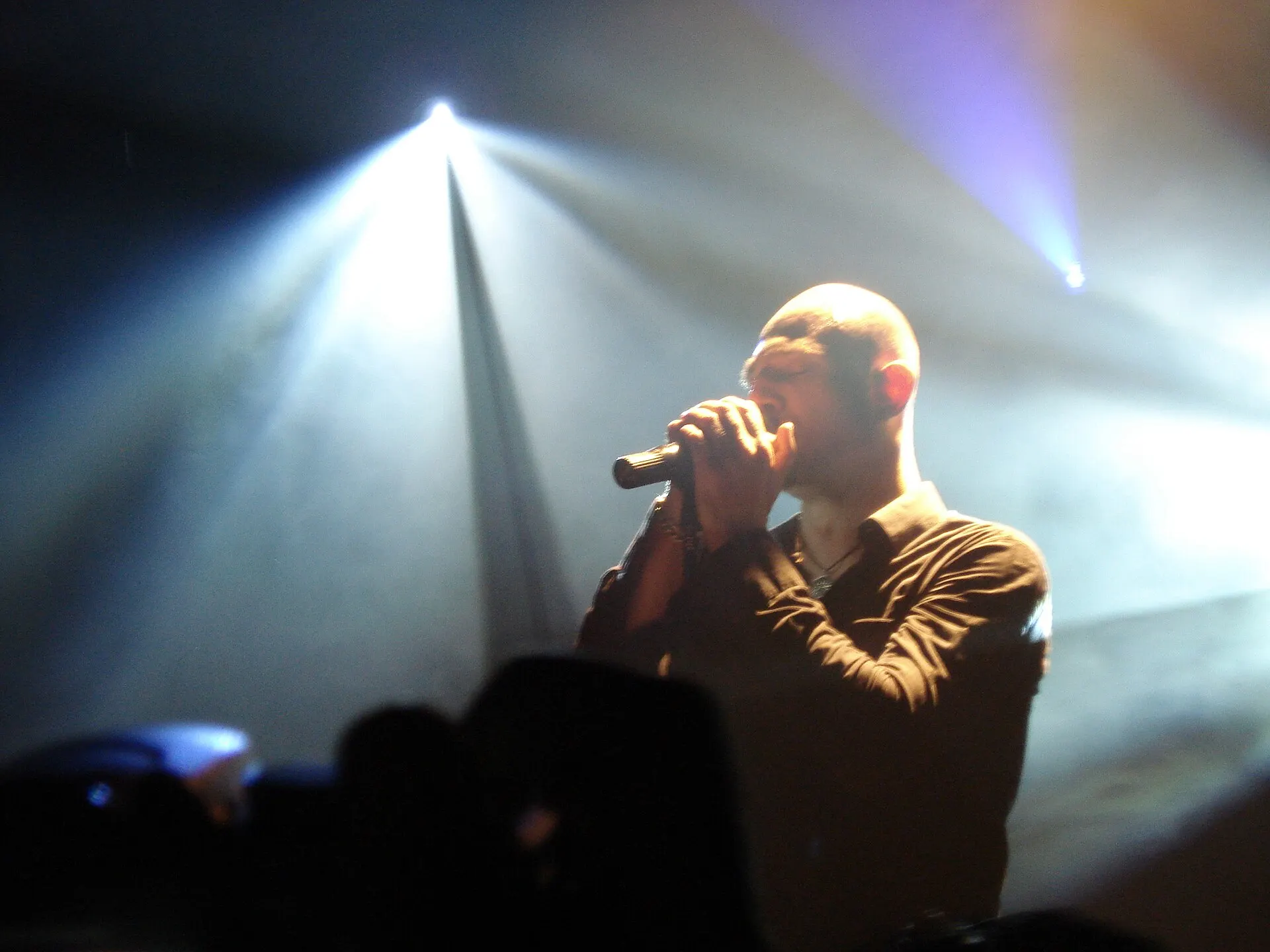 A singer on a dark stage lit by spotlight beams